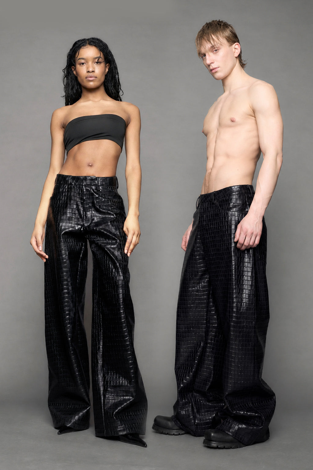 Two models wearing baggy suiting pants in black croc texture against a gray background