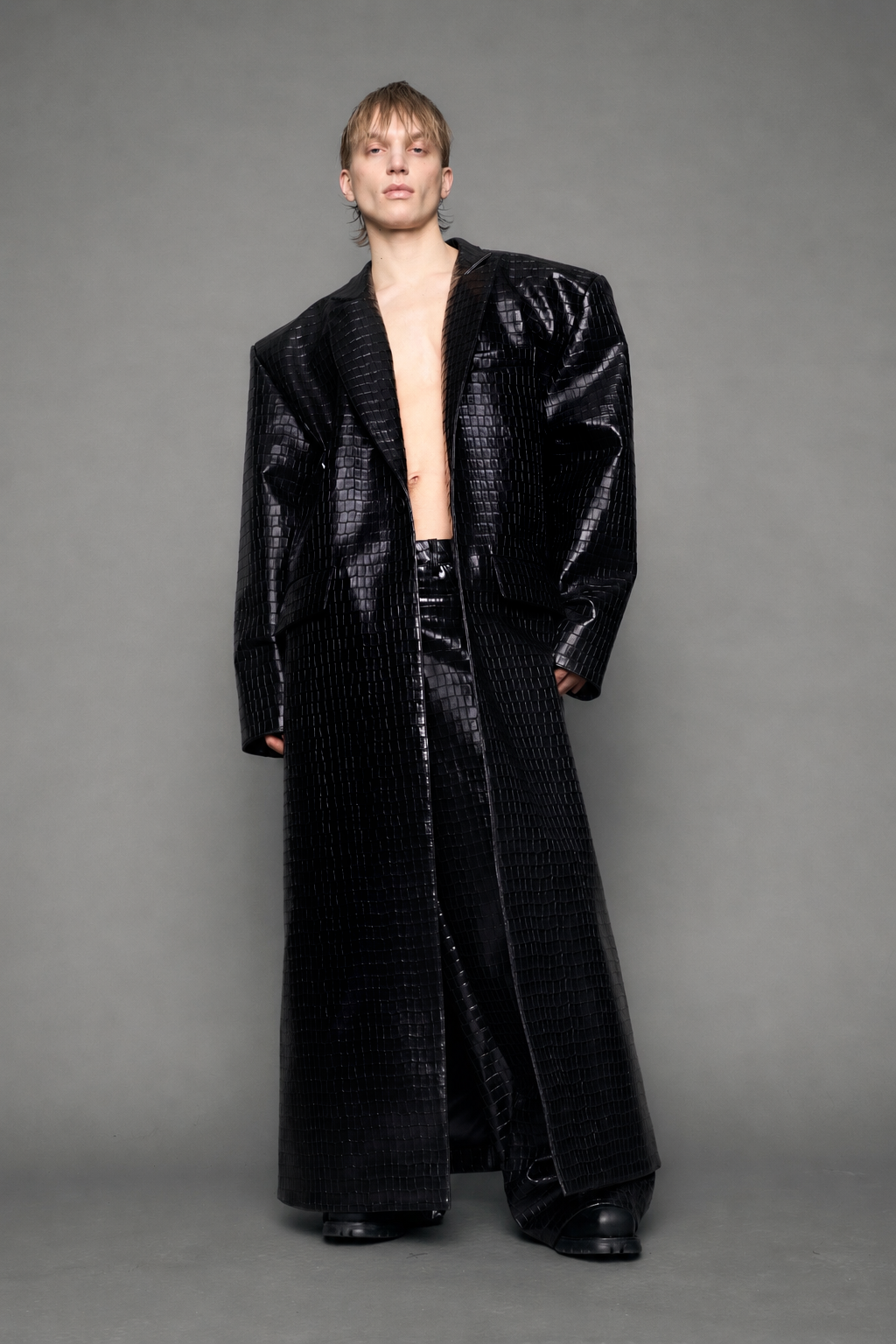 model wearing long black croc textured coat against a gray background