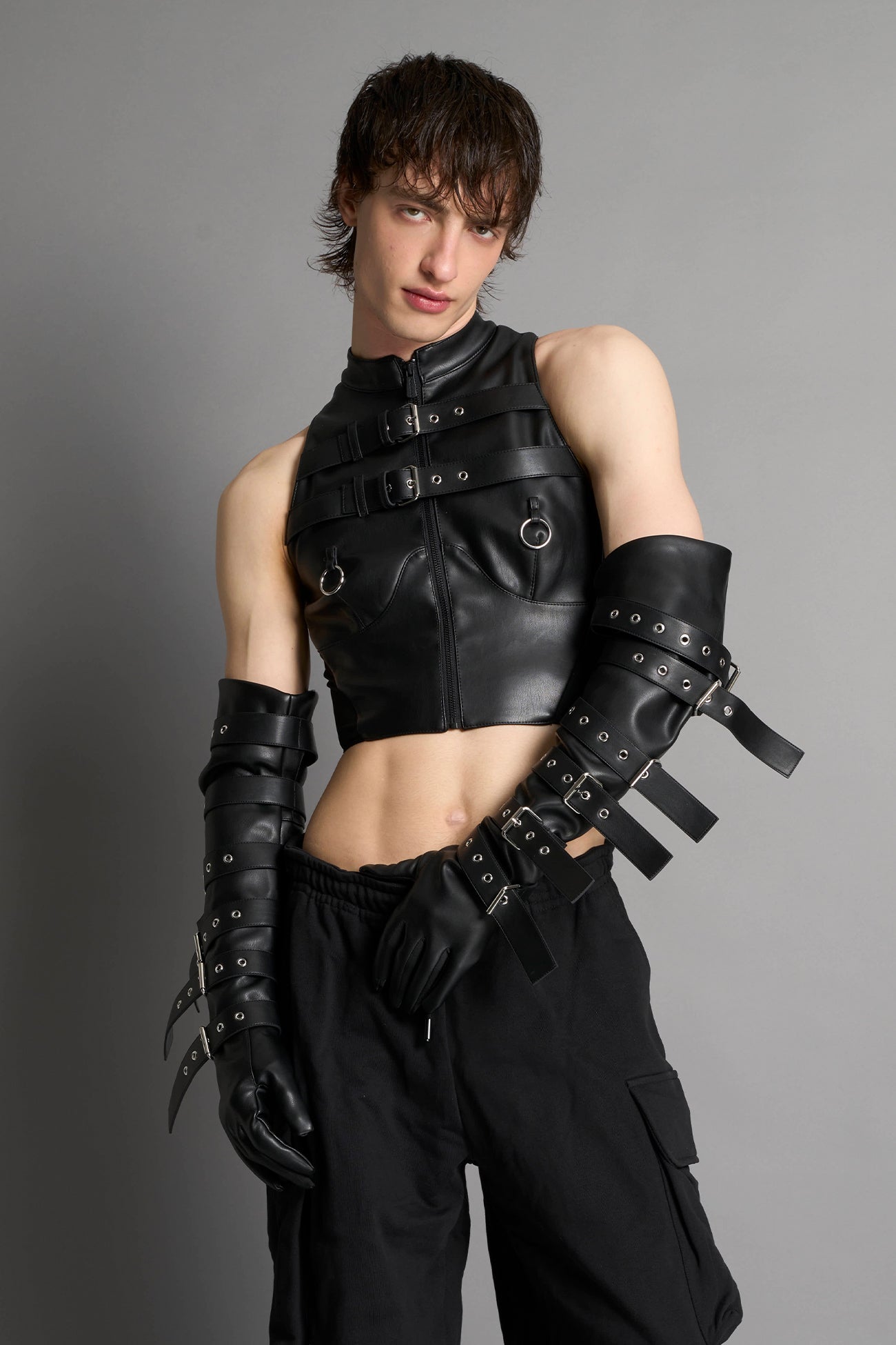 Namilia male model Piercing Top in black vegan leather featuring silver metal ring details, cutout design, and edgy Y2K-inspired crop top style. front view