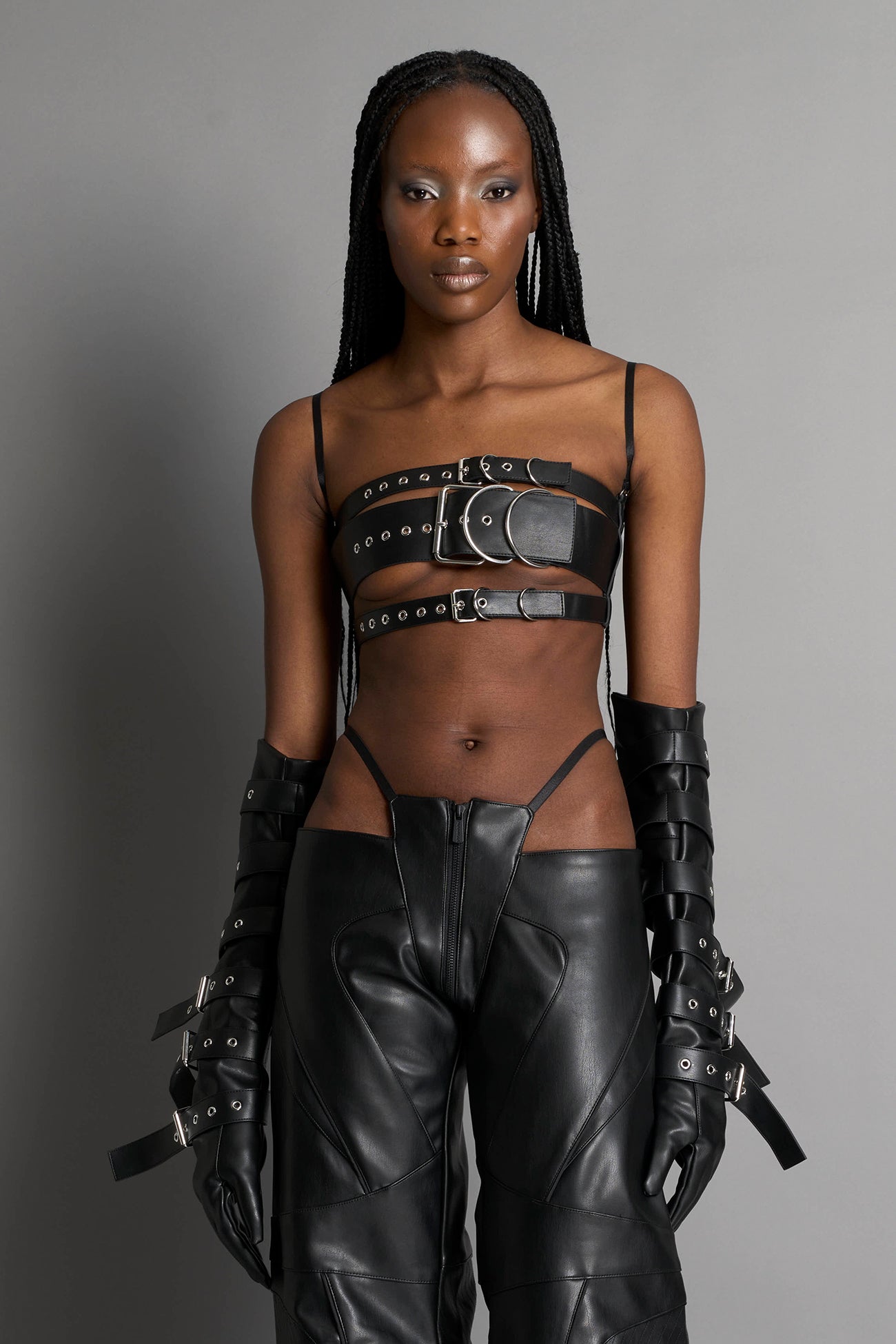 Black vegan leather belt top with three adjustable grommet straps, oversized metal buckles, and circular hardware – edgy bondage-inspired crop top for festival or clubwear.