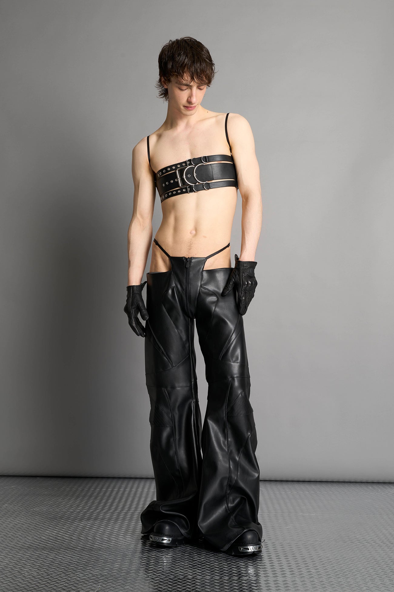 Low-rise flared pants in black faux leather with bold side cut-outs and thong strap detailing. Featuring moto-style paneling, front zip closure, and a sculpted fit. A statement piece for rave, nightlife, and runway-inspired looks.