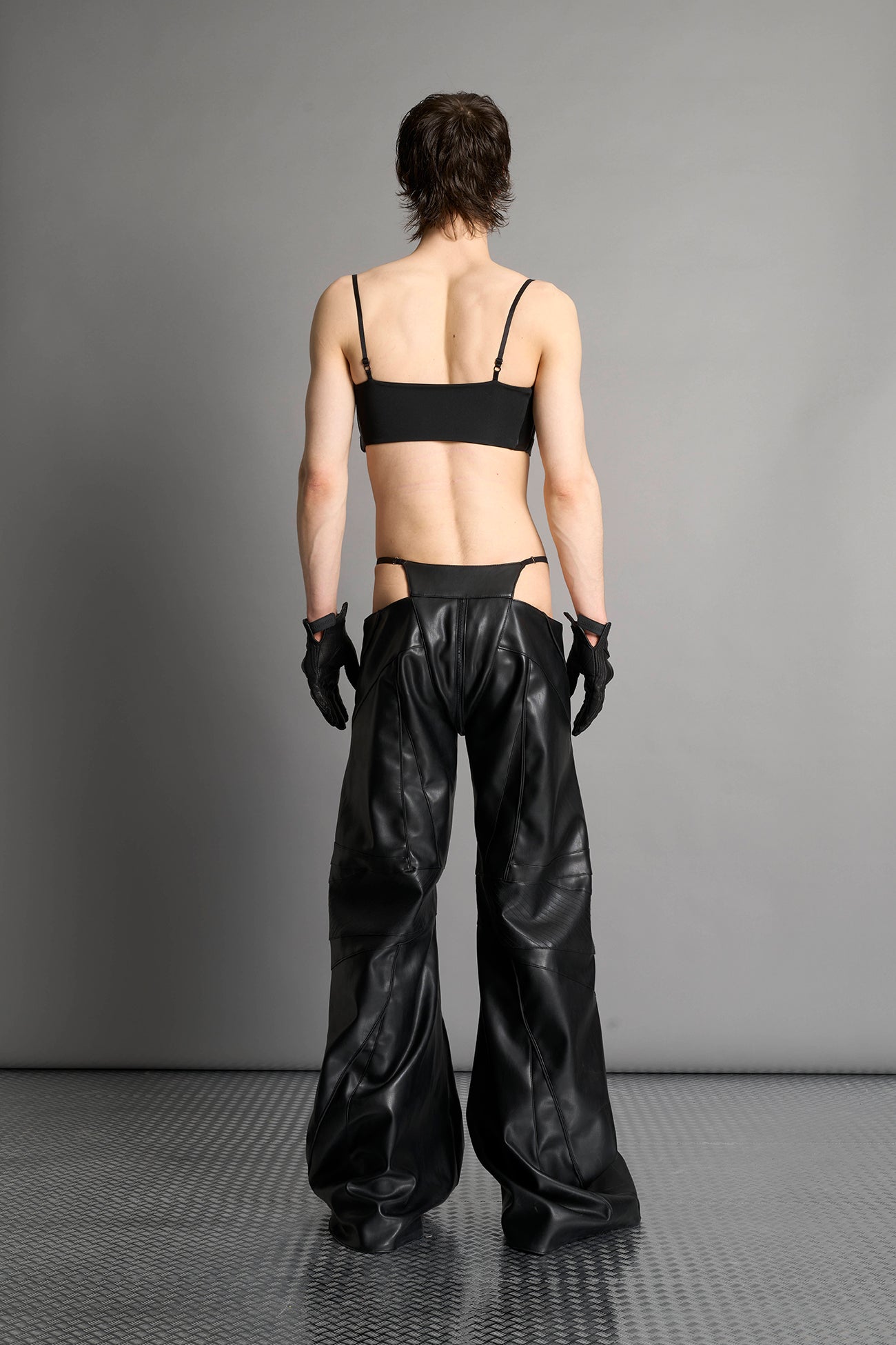 Low-rise flared pants in black faux leather with bold side cut-outs and thong strap detailing. Featuring moto-style paneling, front zip closure, and a sculpted fit. A statement piece for rave, nightlife, and runway-inspired looks.