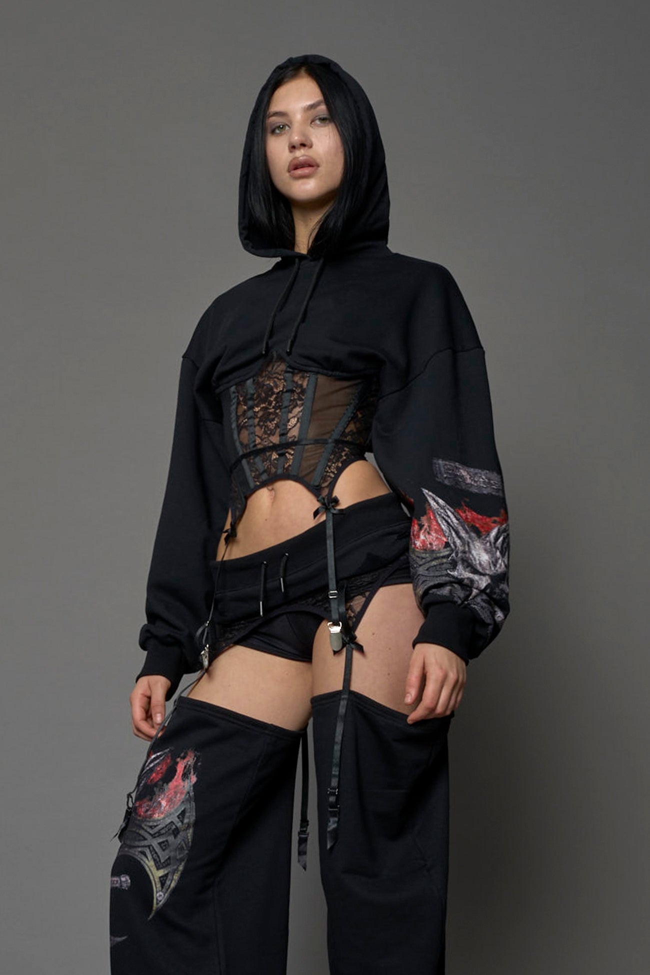 female model wearing a lingerie-inspired black hoodie with a lace corset and a goth-inspired print