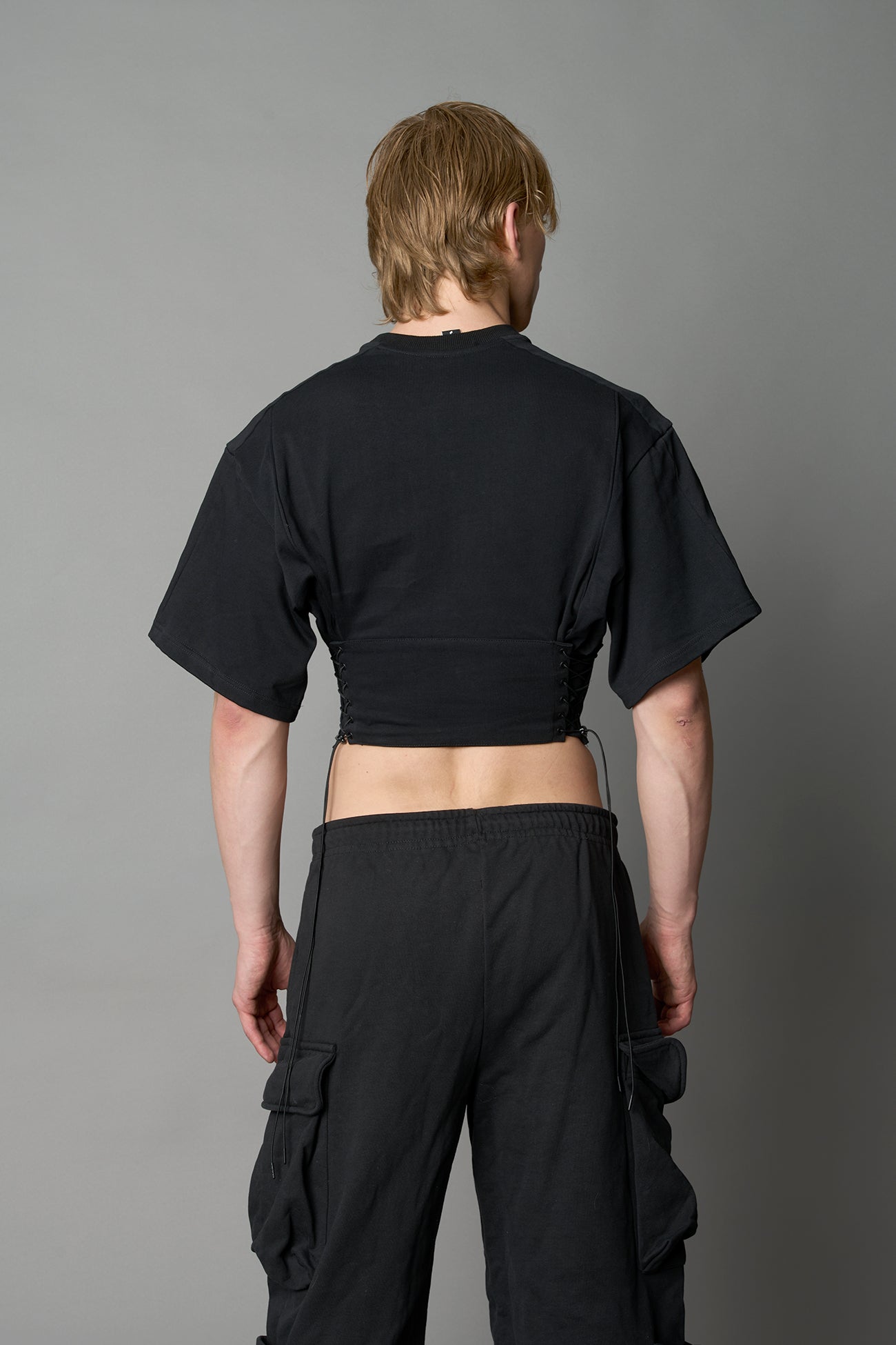 Front view of model in black Namilia Corset-T shirt with sculpted corset-style waist, curved hemline, and oversized sleeves, styled with leather mini skirt and moto boots.