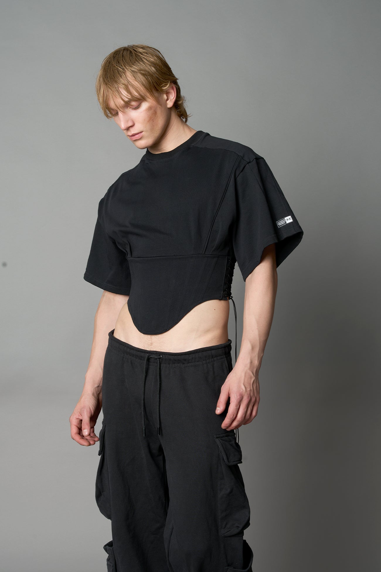 Front view of model in black Namilia Corset-T shirt with sculpted corset-style waist, curved hemline, and oversized sleeves, styled with leather mini skirt and moto boots.