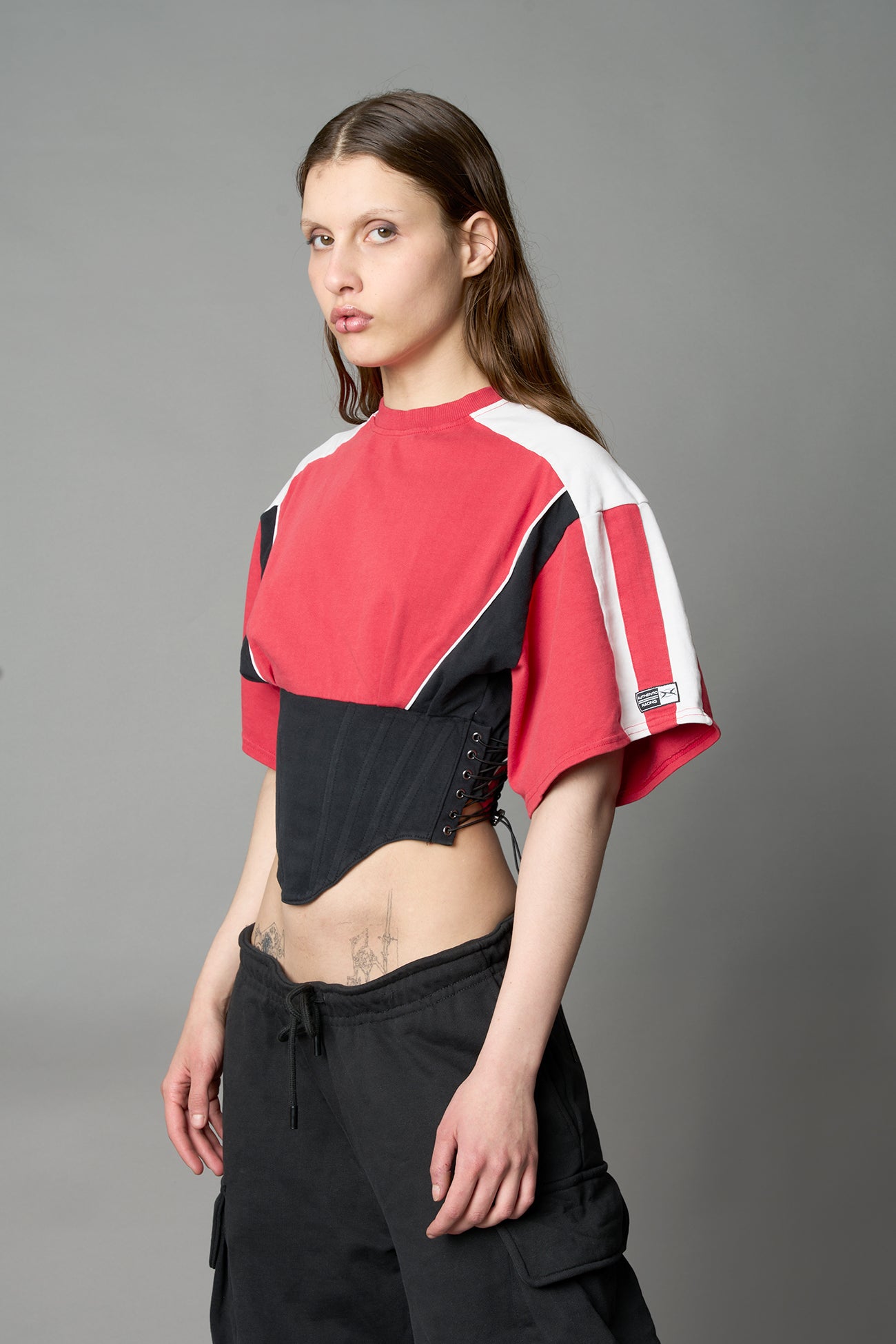 Front view of model in red Namilia Corset-T shirt with sculpted corset-style waist, curved hemline, and oversized sleeves,