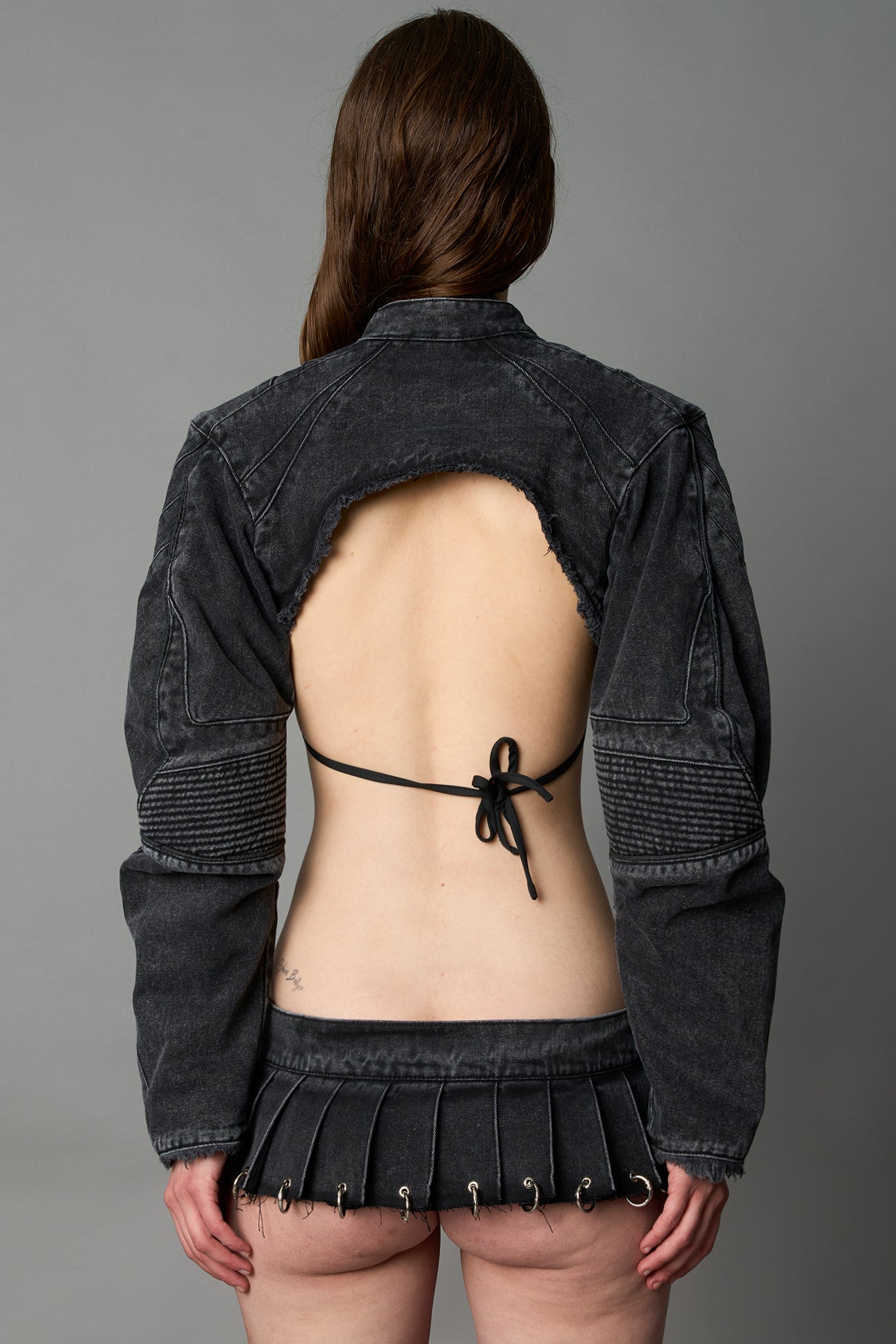 Model in ultra-cropped black washed denim bolero jacket with front zipper, raw frayed edges, choker neckline, and sculpted biker sleeves