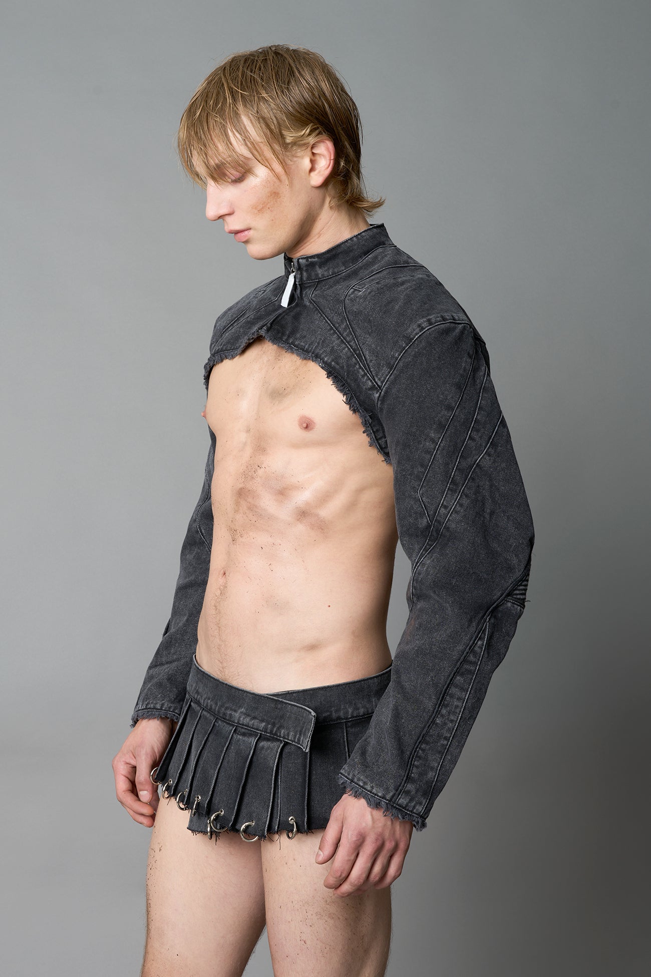 Model in ultra-cropped black washed denim bolero jacket with front zipper, raw frayed edges, choker neckline, and sculpted biker sleeves