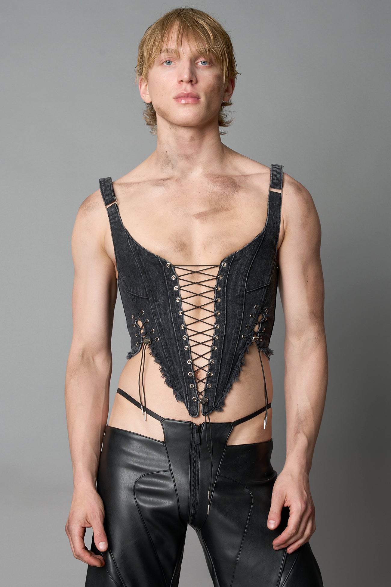 Model wearing black washed denim corset top with plunging neckline, lace-up front and sides, raw frayed hem, and structured fit