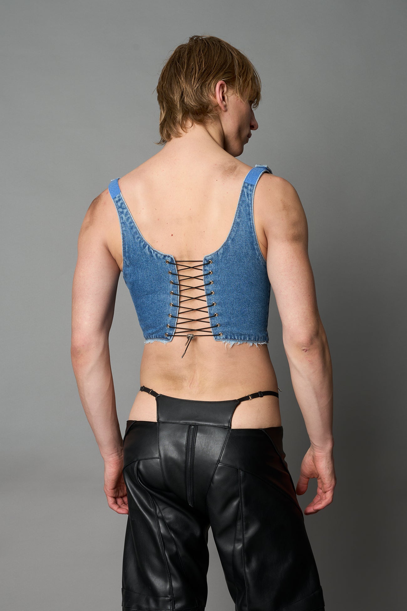 Model wearing blue washed denim corset top with plunging neckline, lace-up front and sides, raw frayed hem, and structured fit