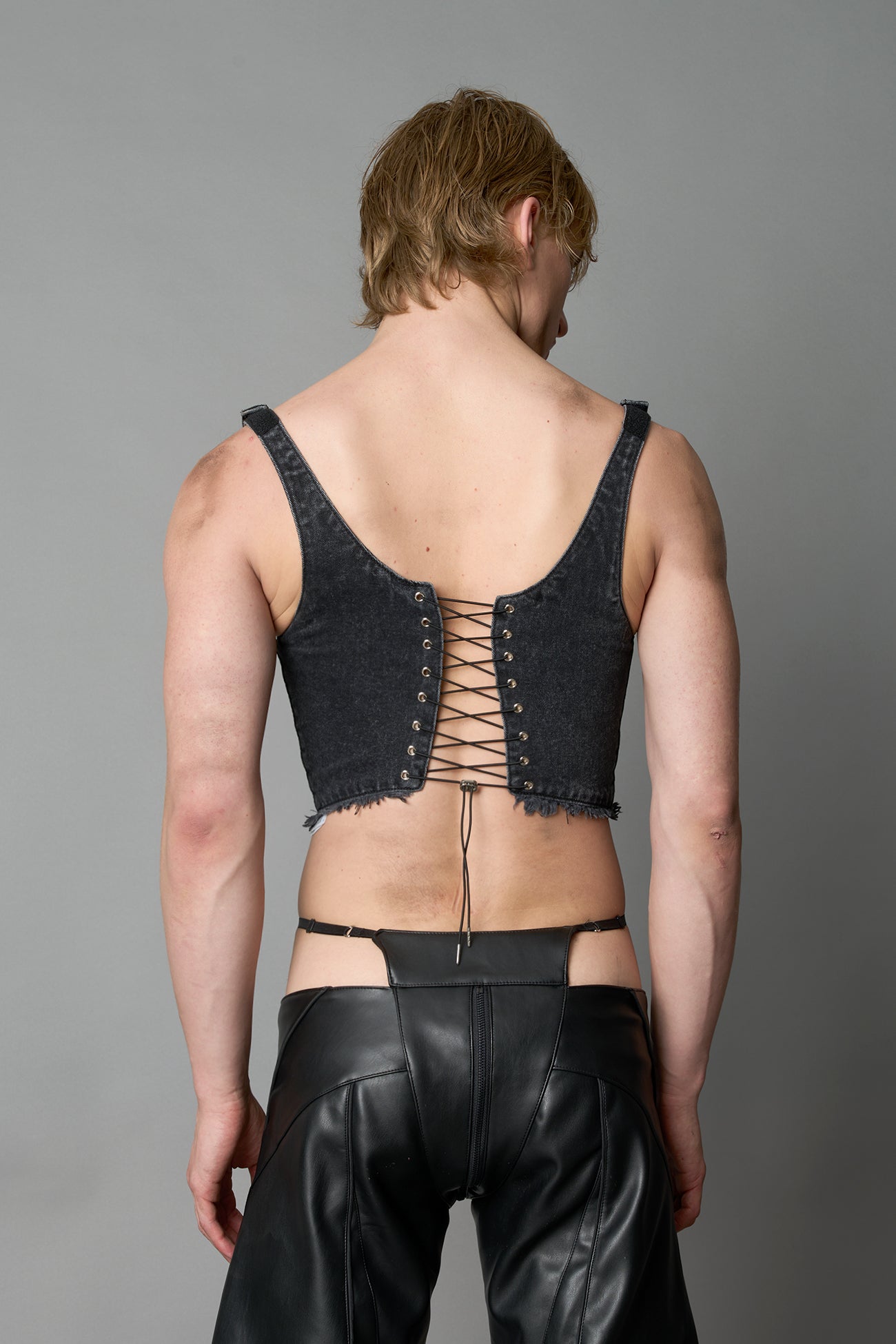 Model wearing black washed denim corset top with plunging neckline, lace-up front and sides, raw frayed hem, and structured fit