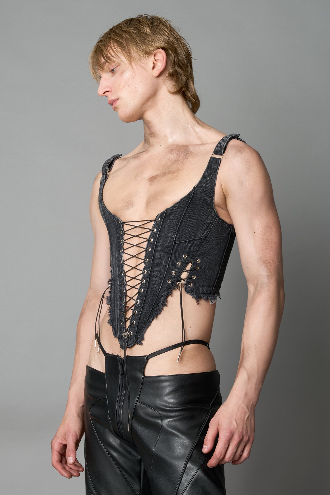 Model wearing black washed denim corset top with plunging neckline, lace-up front and sides, raw frayed hem, and structured fit
