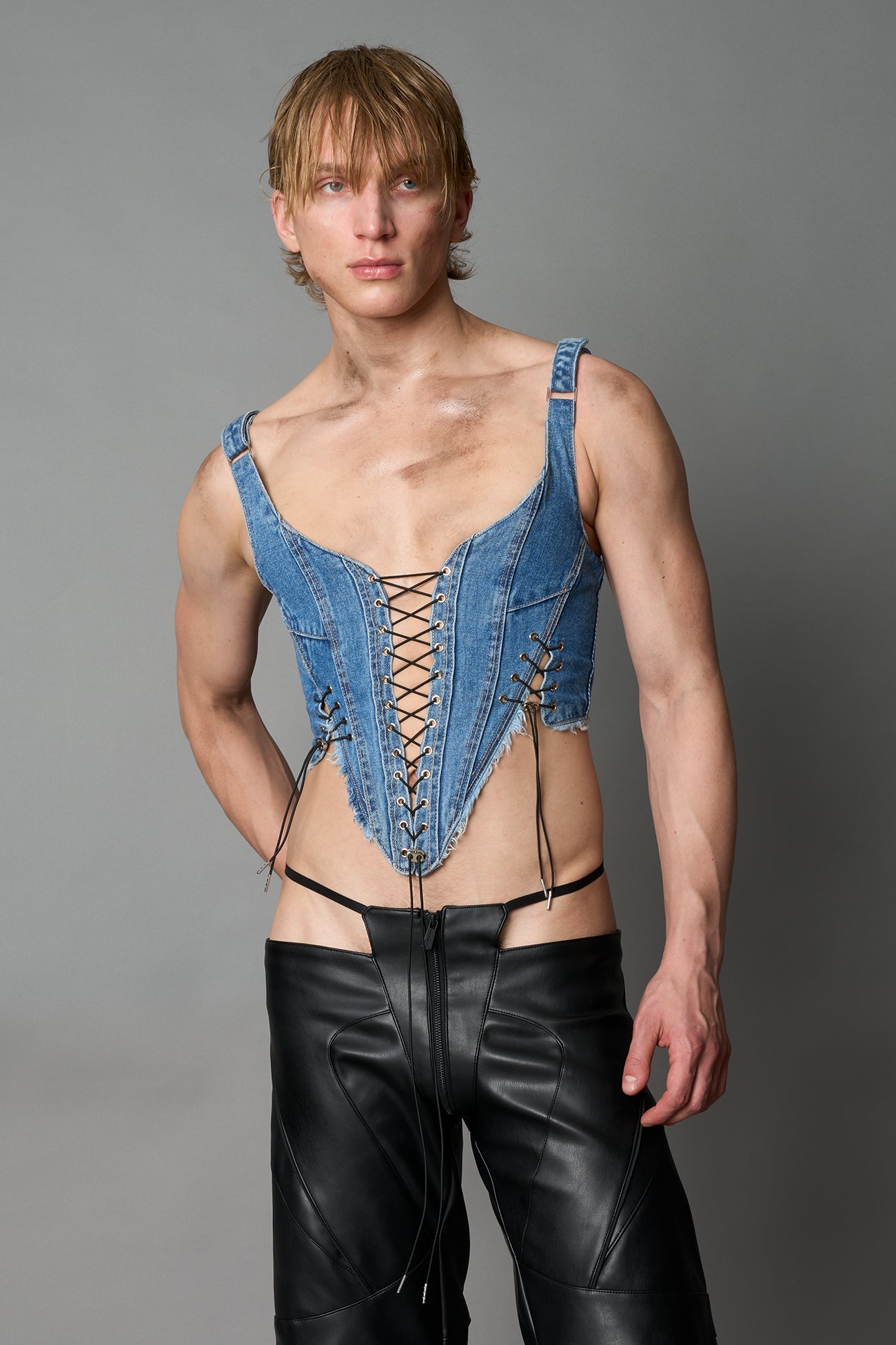 Model wearing blue washed denim corset top with plunging neckline, lace-up front and sides, raw frayed hem, and structured fit