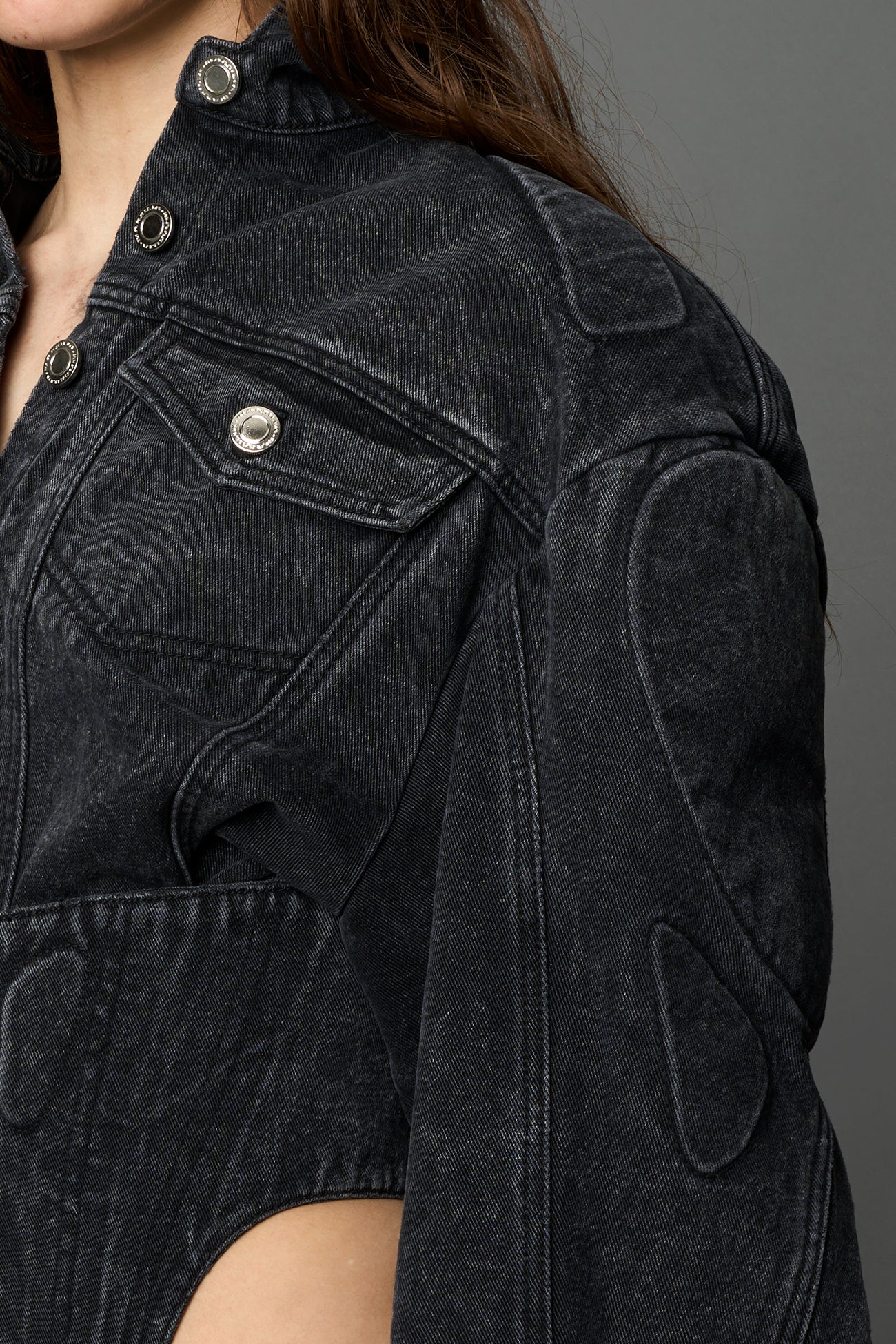 Side view of model wearing black washed denim biker corset jacket with sculpted sleeves and waist cutouts