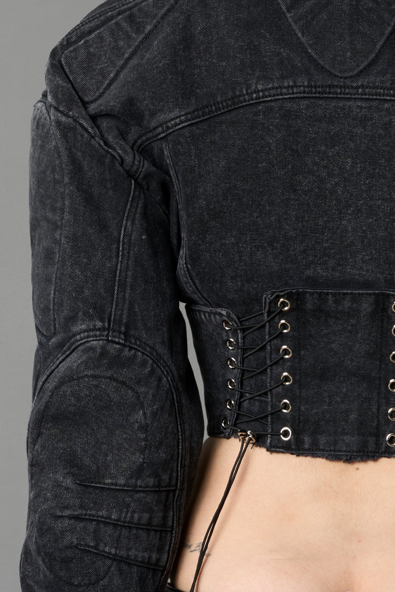 model wearing washed black denim jacket with structured corset waist and moto-style silhouette