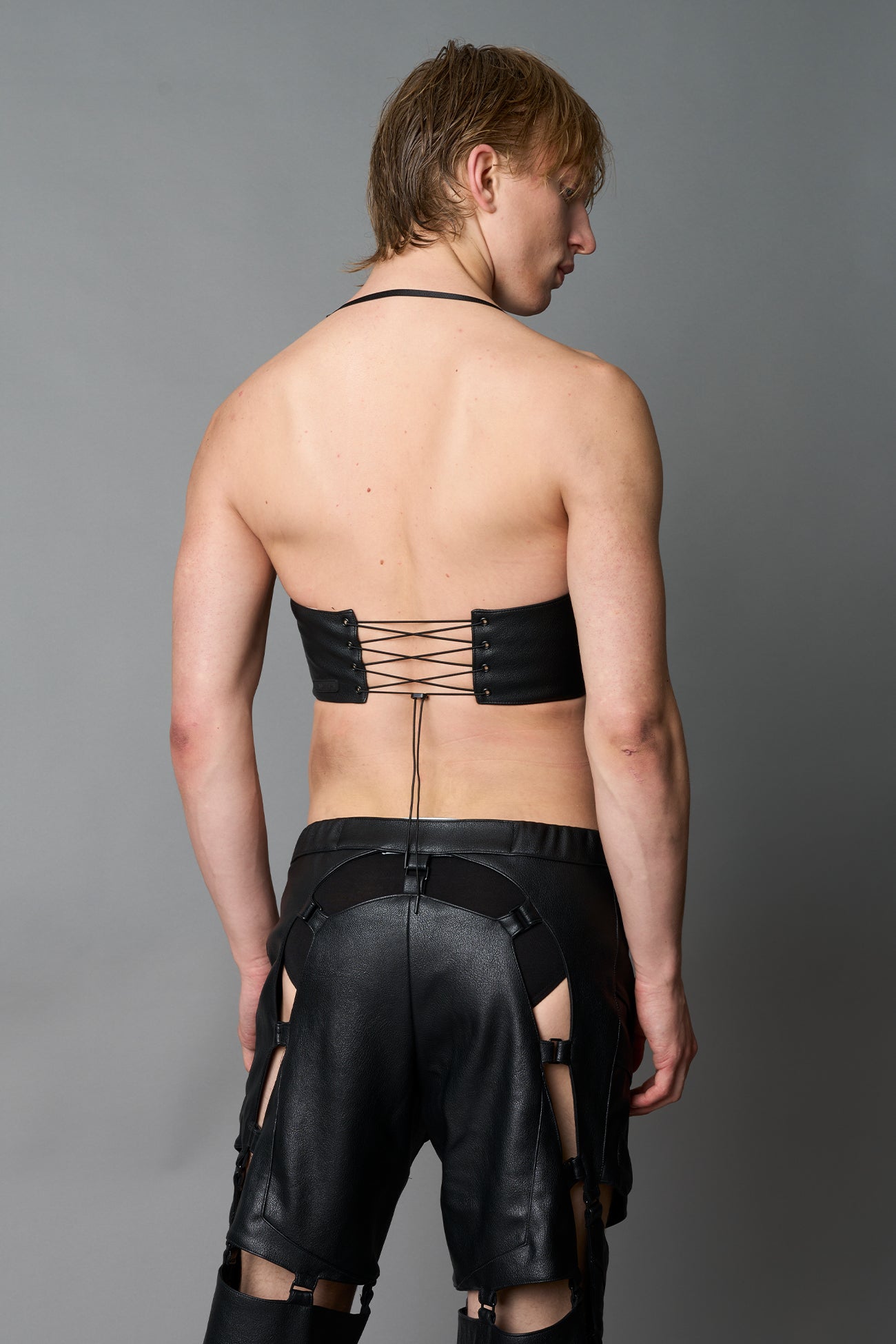 Model in bold black vegan leather statement halter top with provocative cup design and front zipper, paired with matching pants – futuristic streetwear look
