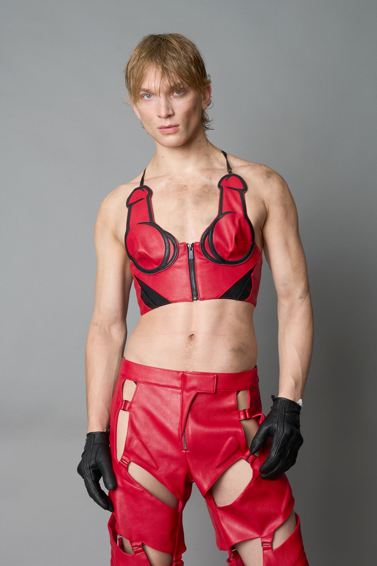 Model in bold red vegan leather statement halter top with provocative cup design and front zipper, paired with matching pants – futuristic streetwear look