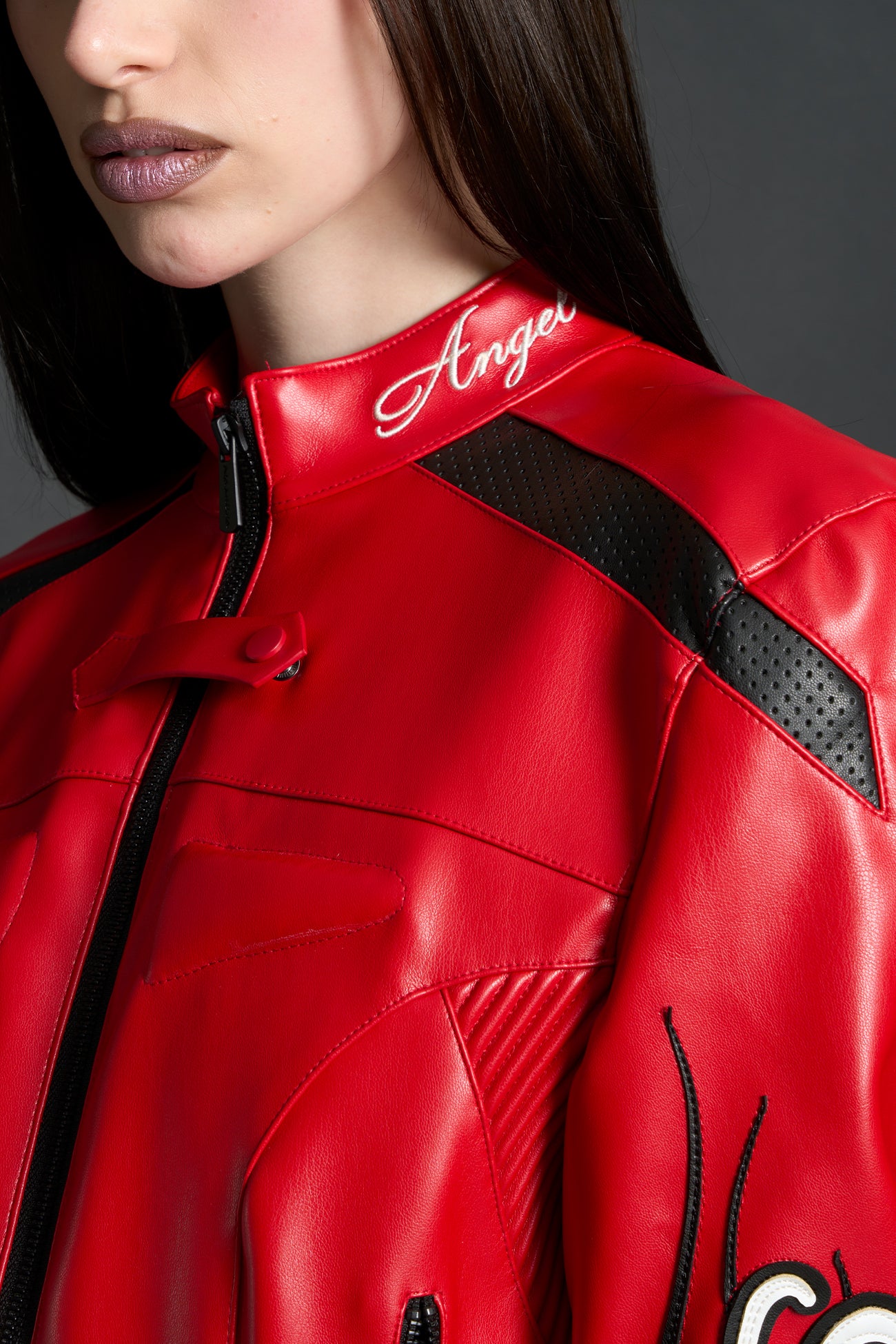 Model wears a motocross jacket-style vegan leather bodysuit with red motocross paneling, padded details, flame graphics, and ‘Hollywood Angel’ embroidery