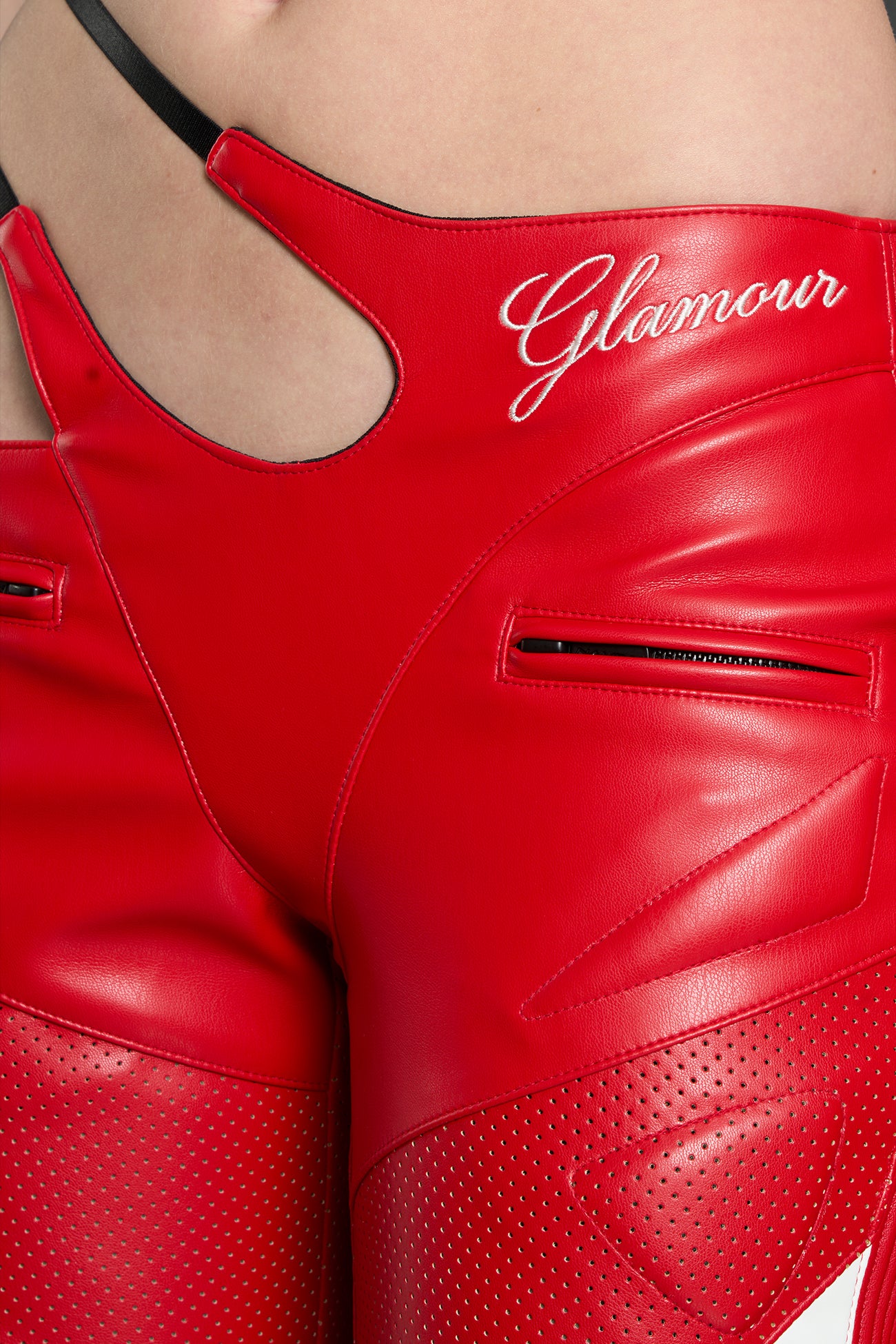 Model wears red vegan leather flare trousers with motocross paneling, padded details, flame and cross stitching, slogan embroidery, and an asymmetric waistband with adjustable elastic thong straps.