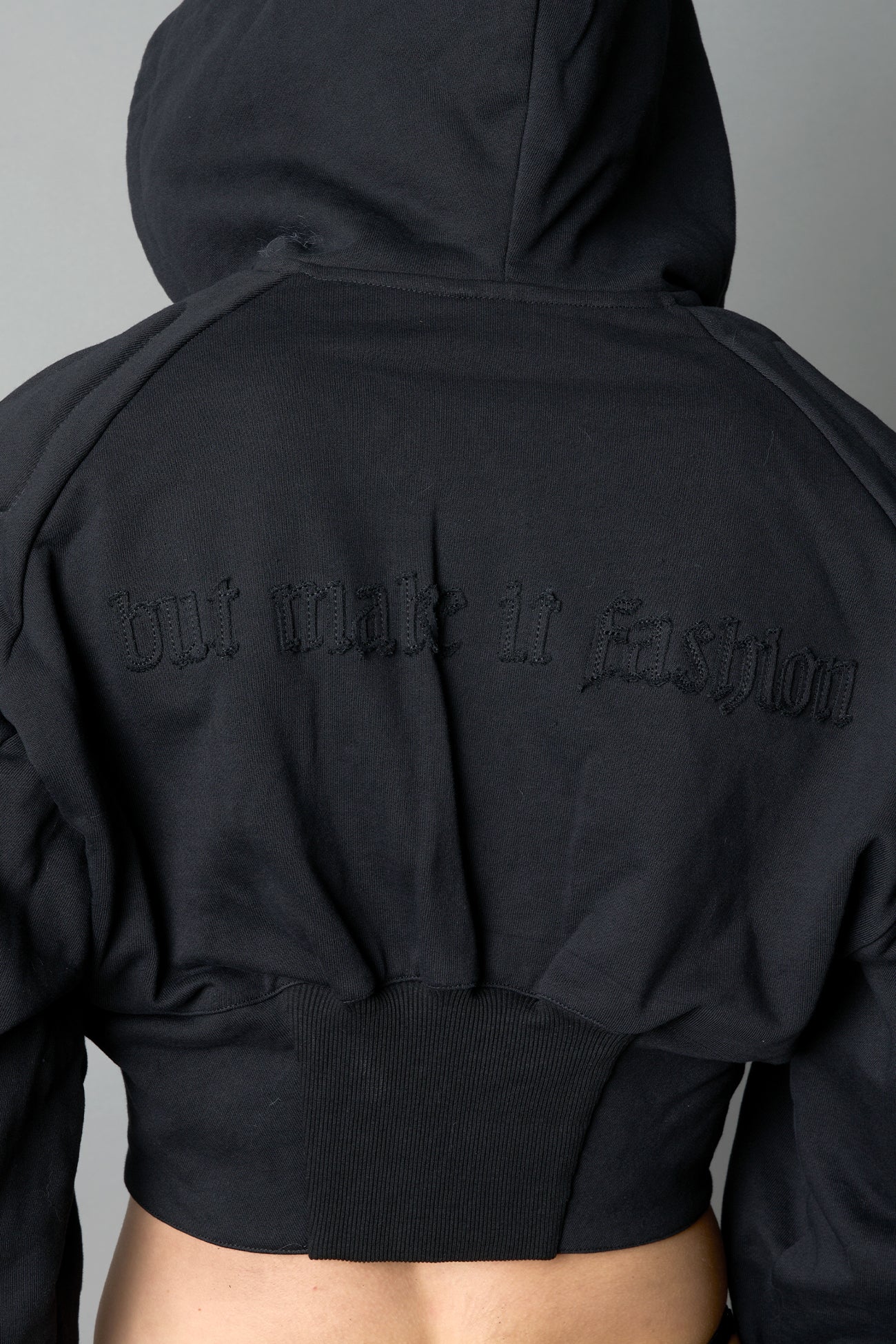 model in a black cropped hoodie featuring structured corset-style paneling embroidered across the chest in tonal black