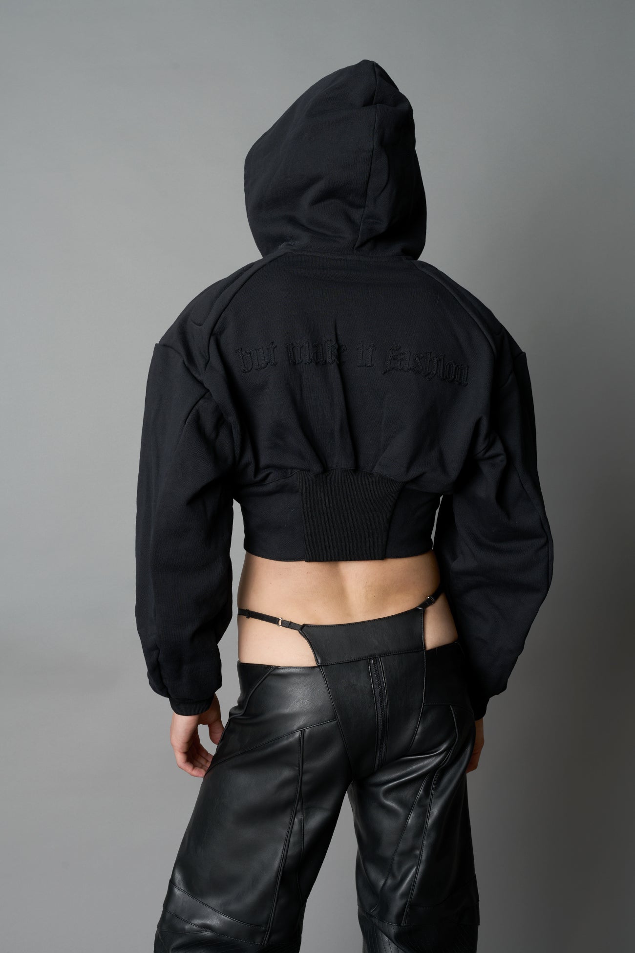 model in a black cropped hoodie featuring structured corset-style paneling embroidered across the chest in tonal black