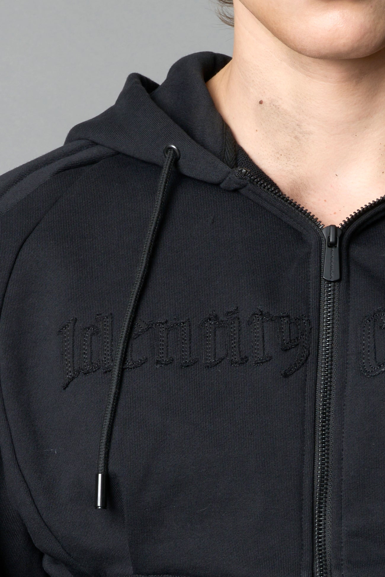 model in a black cropped hoodie featuring structured corset-style paneling embroidered across the chest in tonal black