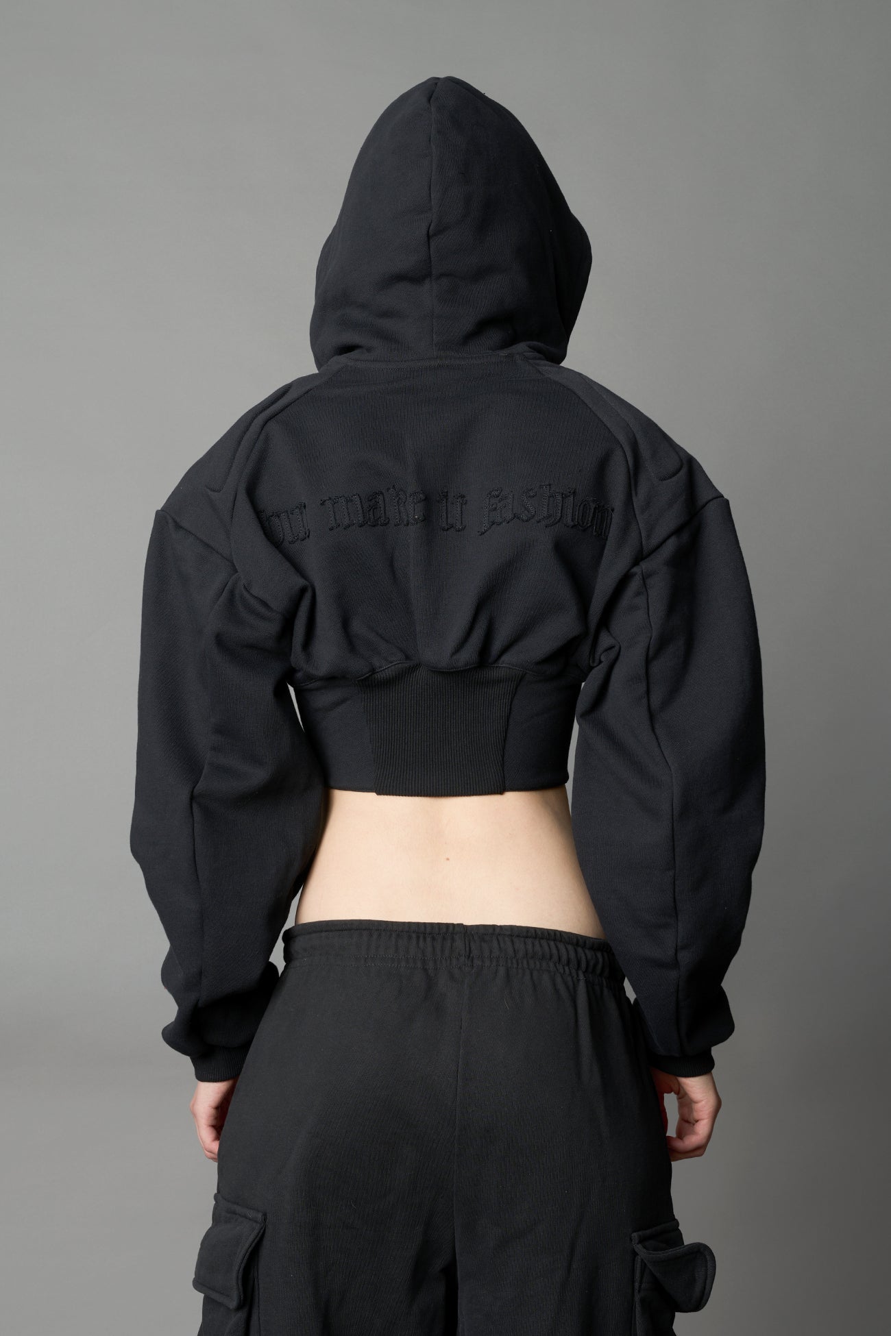 model in a black cropped hoodie featuring structured corset-style paneling embroidered across the chest in tonal black