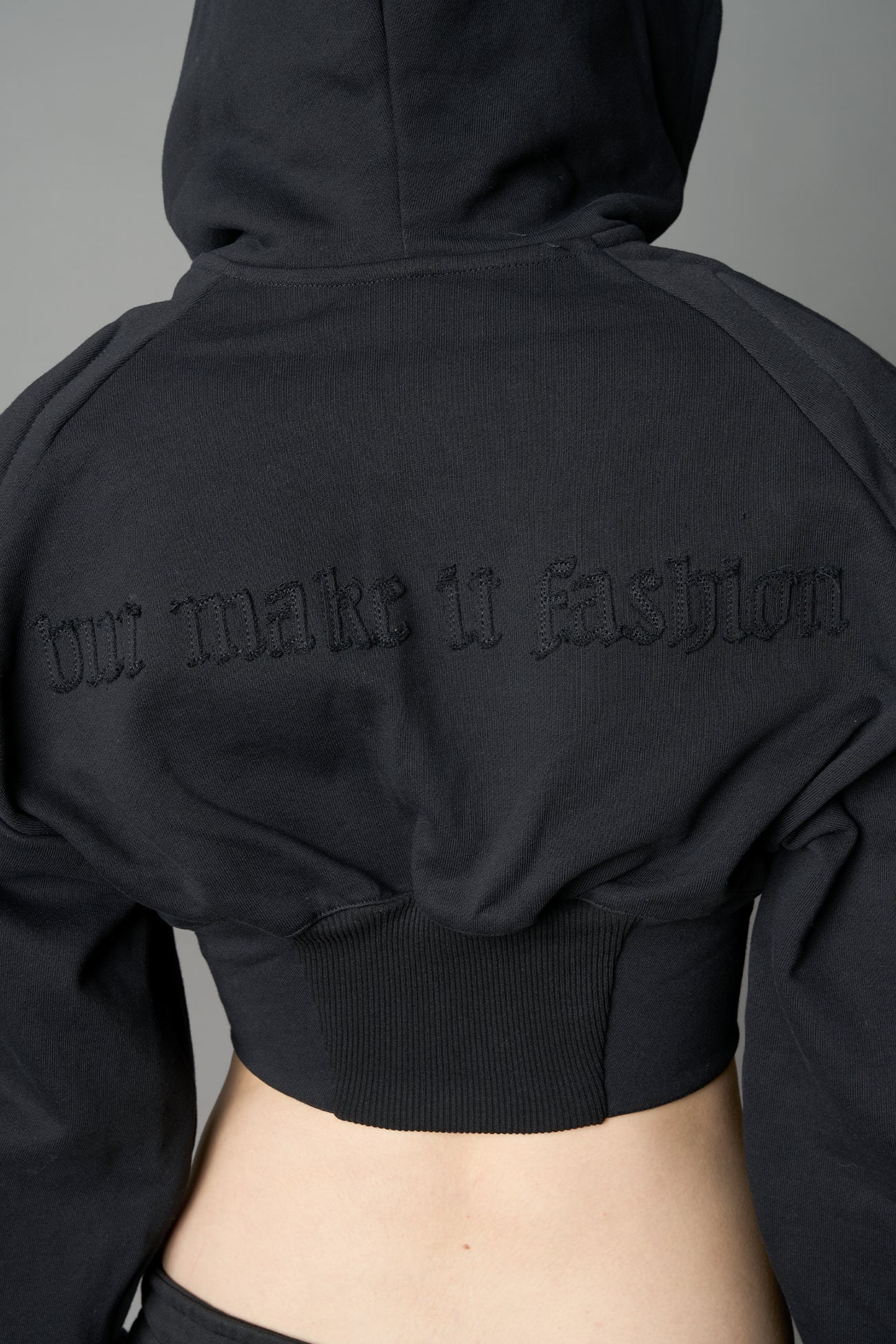 model in a black cropped hoodie featuring structured corset-style paneling embroidered across the chest in tonal black