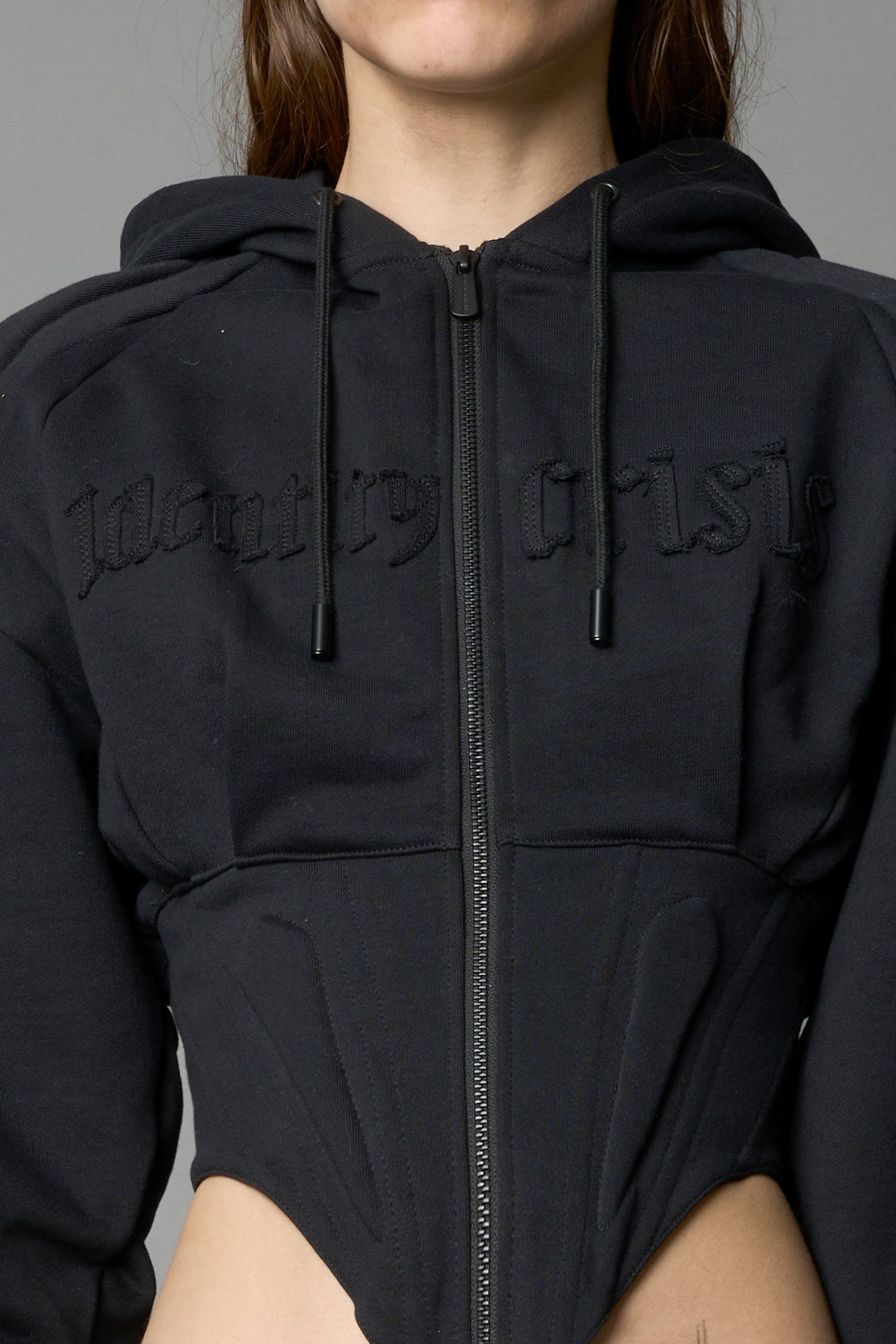 model in a black cropped hoodie featuring structured corset-style paneling embroidered across the chest in tonal black