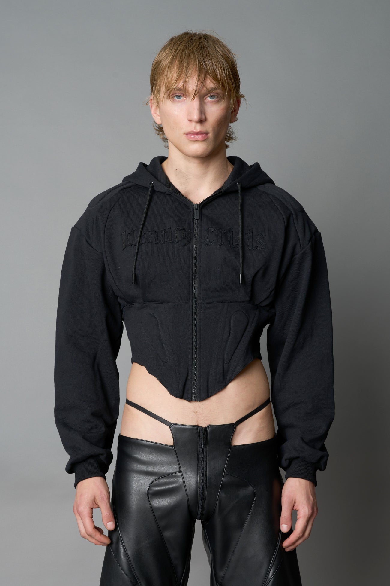 model in a black cropped hoodie featuring structured corset-style paneling embroidered across the chest in tonal black