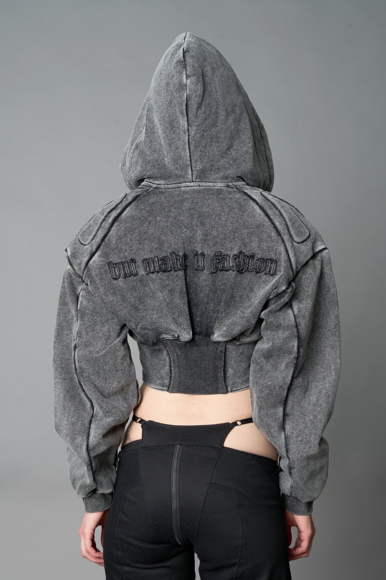 model in a washed-black cropped hoodie featuring structured corset-style paneling embroidered across the chest in tonal black