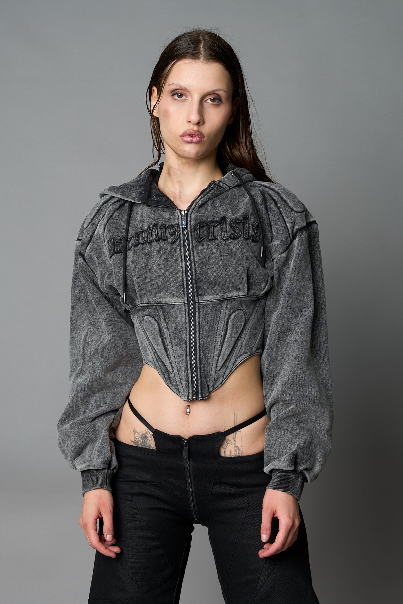 model in a washed-black cropped hoodie featuring structured corset-style paneling embroidered across the chest in tonal black