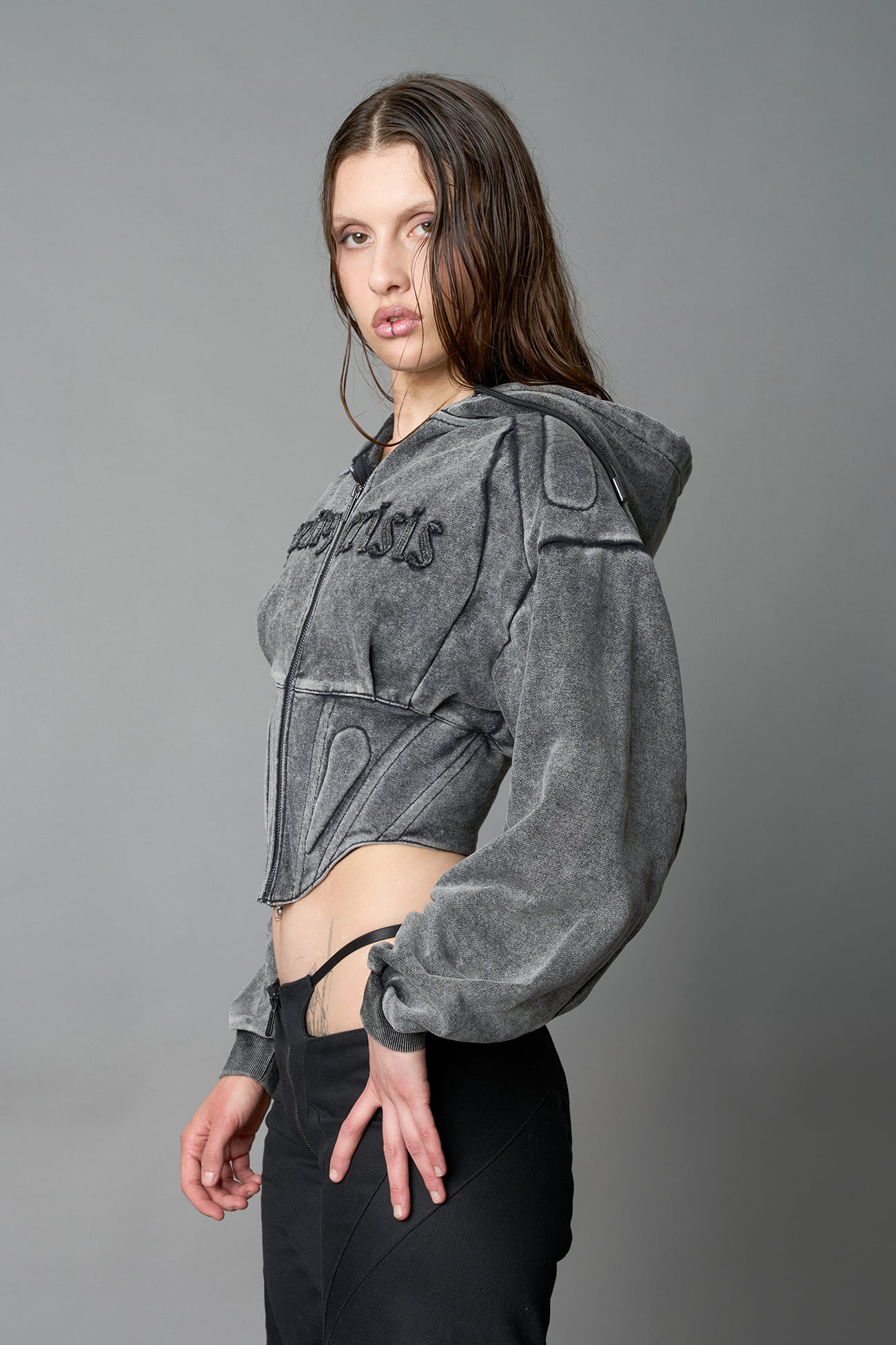 model in a washed-black cropped hoodie featuring structured corset-style paneling embroidered across the chest in tonal black