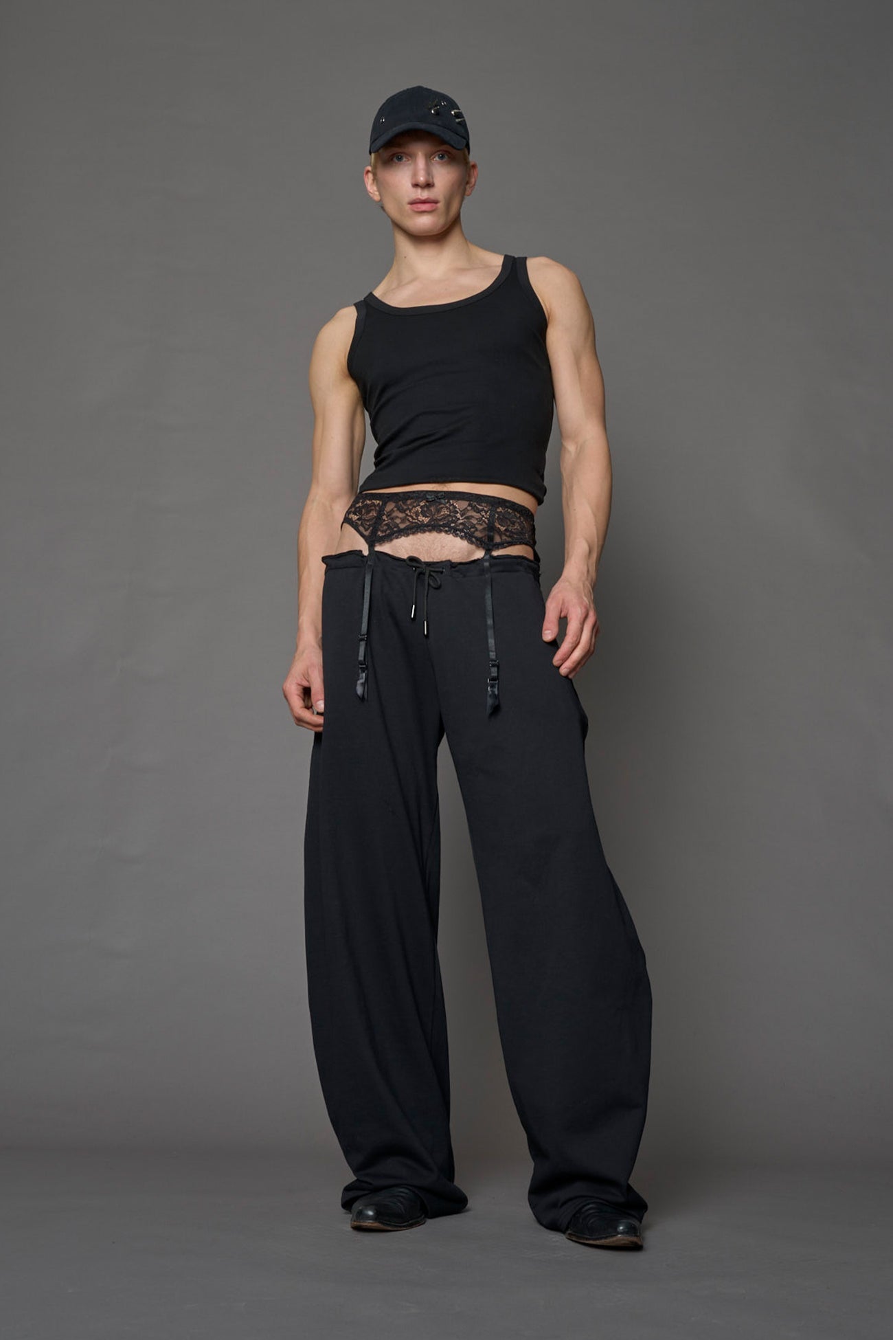 male model wearing a black low waist jogger with a lace suspender belt