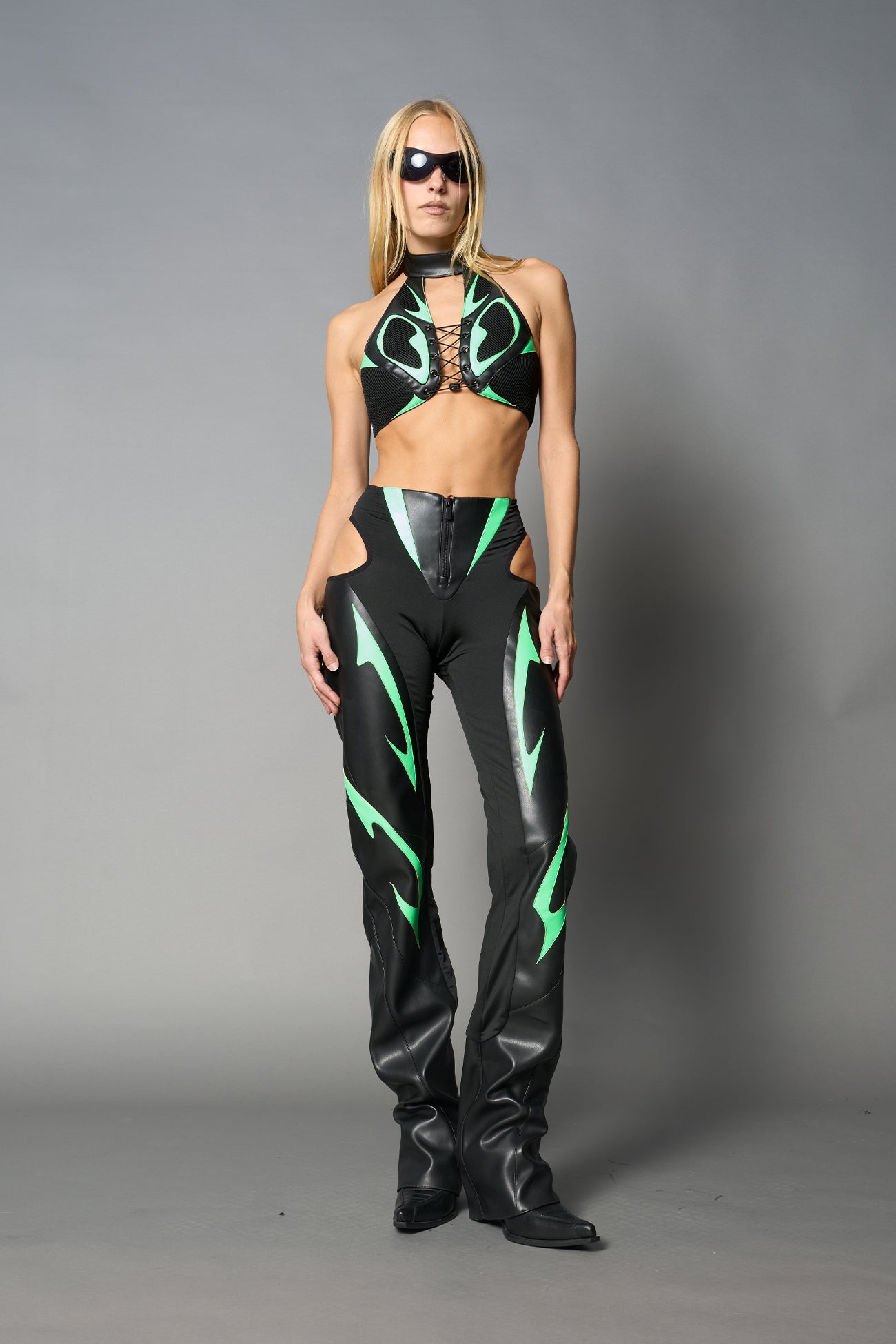 Green cut-out flare pants with graphic details, vegan leather panels, and low-rise waist – edgy motocross-inspired trousers for men’s streetwear or festival looks.
