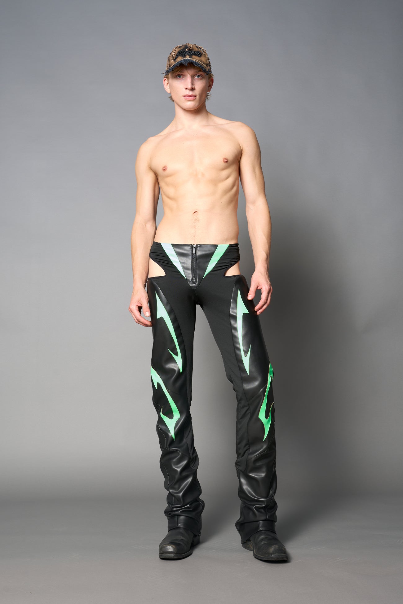 Green cut-out flare pants with graphic details, vegan leather panels, and low-rise waist – edgy motocross-inspired trousers for men’s streetwear or festival looks.