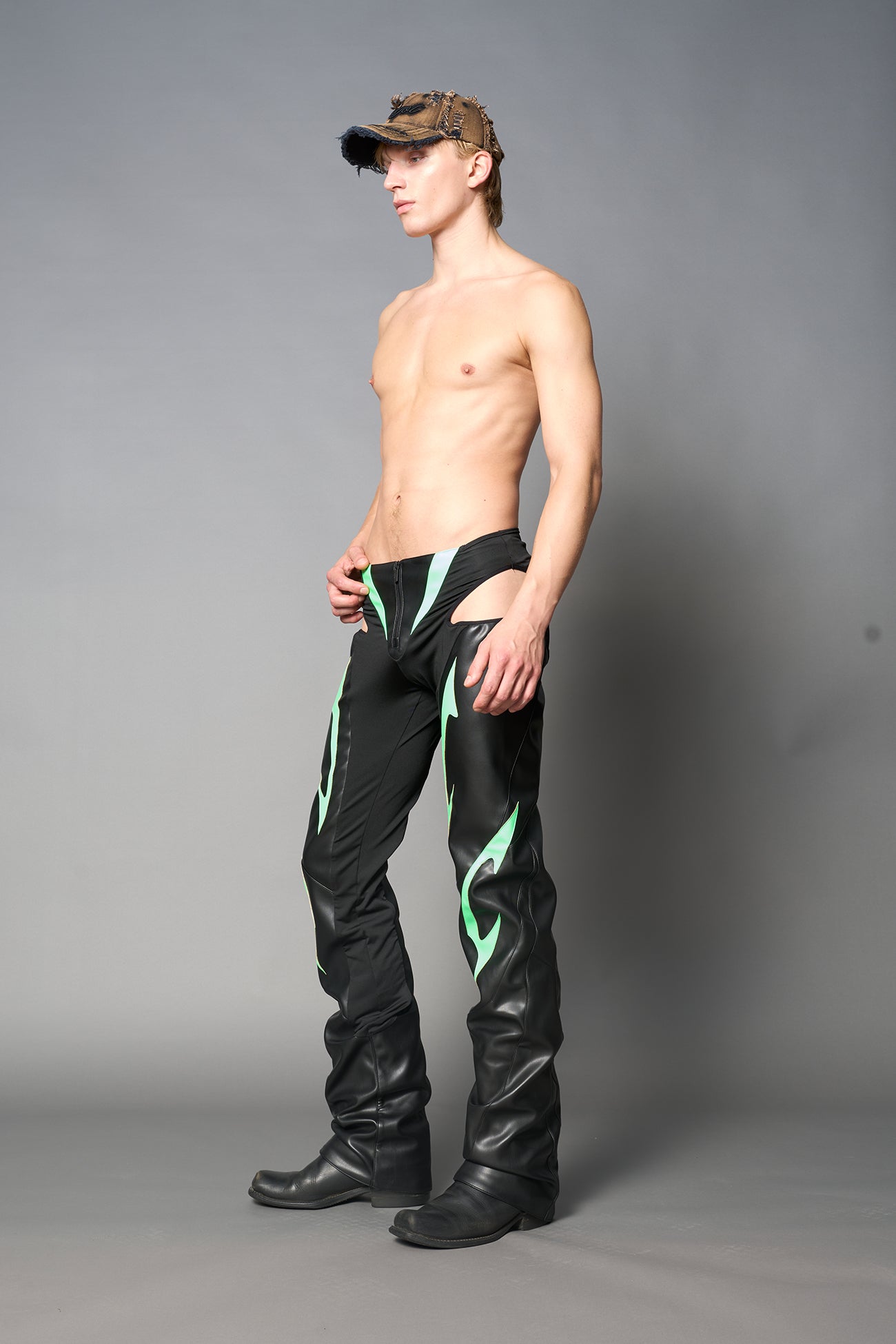 Green cut-out flare pants with graphic details, vegan leather panels, and low-rise waist – edgy motocross-inspired trousers for men’s streetwear or festival looks.