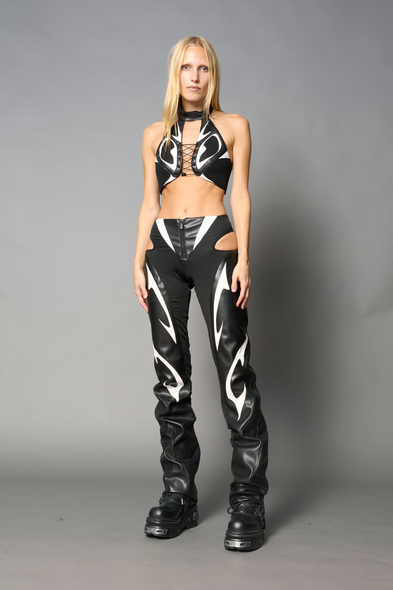 white cut-out flare pants with graphic details, vegan leather panels, and low-rise waist – edgy motocross-inspired trousers for men’s streetwear or festival looks.