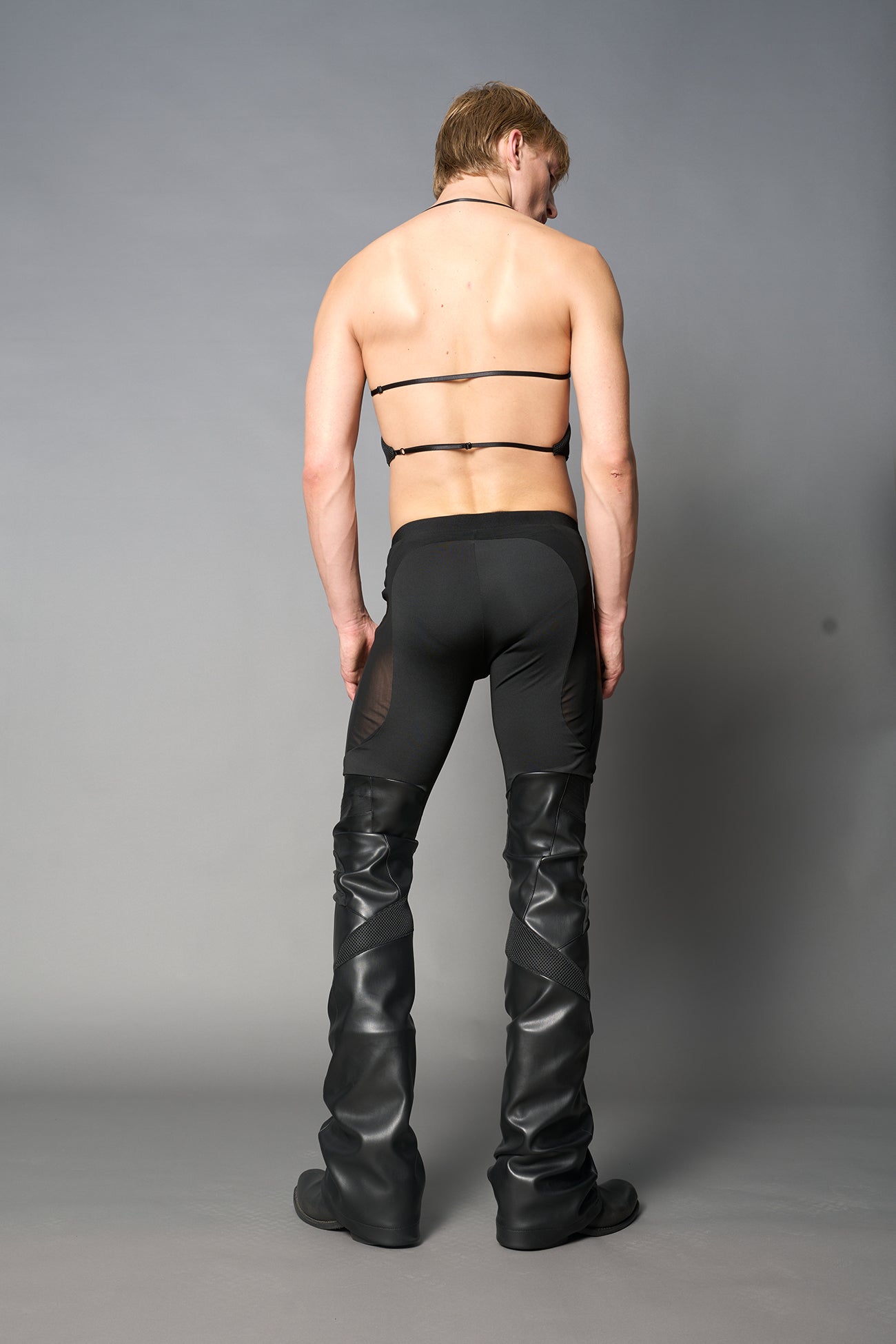 Model wearing high-waisted black vegan leather pants with mesh cutouts, moto-inspired paneling, and flared stacked legs – edgy streetwear trousers styled with chunky platform boots