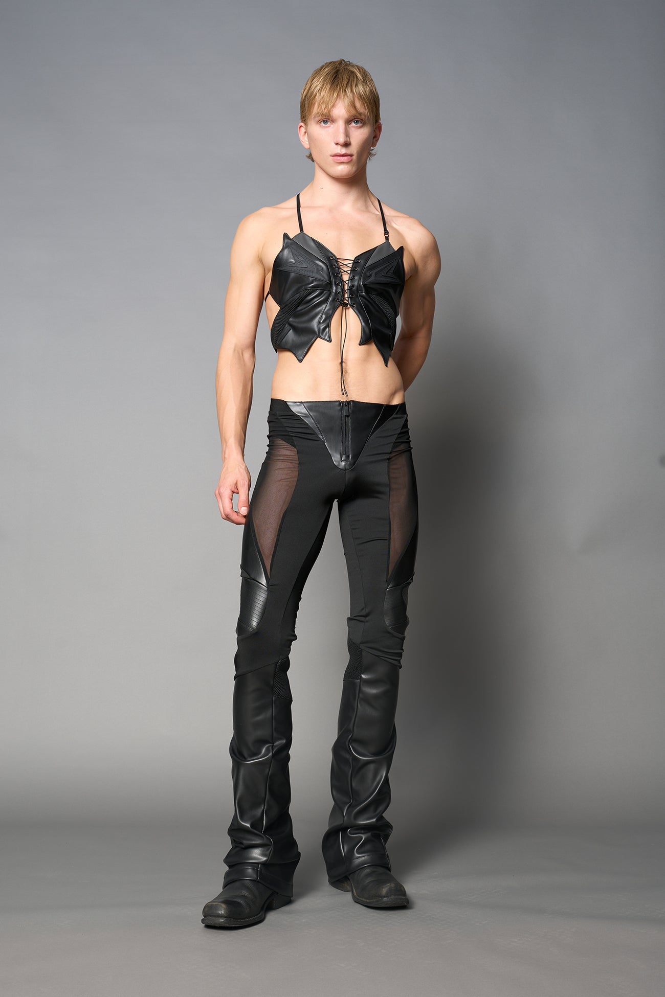 Model wearing high-waisted black vegan leather pants with mesh cutouts, moto-inspired paneling, and flared stacked legs – edgy streetwear trousers styled with chunky platform boots