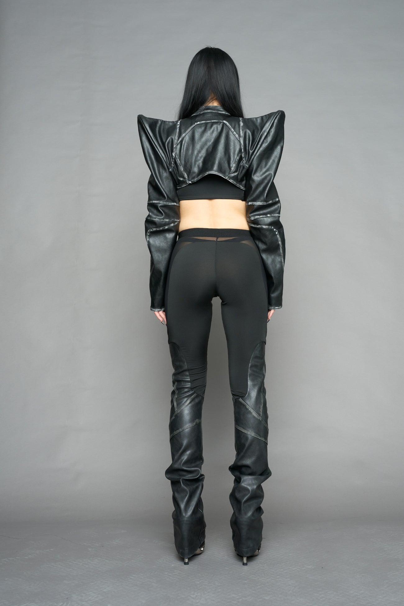 Model wearing high-waisted black washed vegan leather pants with mesh cutouts, moto-inspired paneling, and flared stacked legs – edgy streetwear trousers styled with chunky platform boots