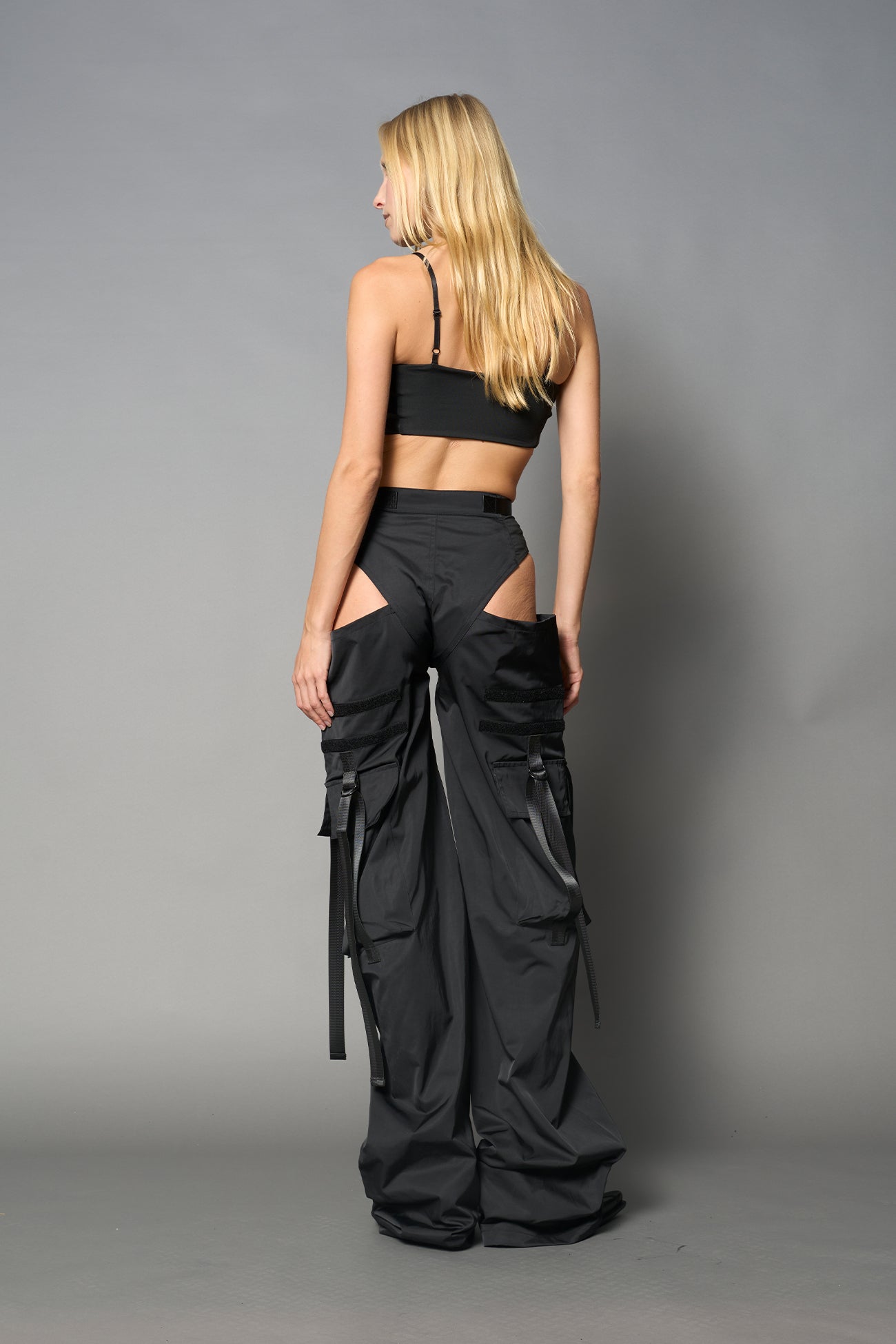 Black nylon cargo trousers with exposed high-cut panty waist, cut-out hips, oversized pockets, and adjustable utility straps – edgy streetwear and festival pants.