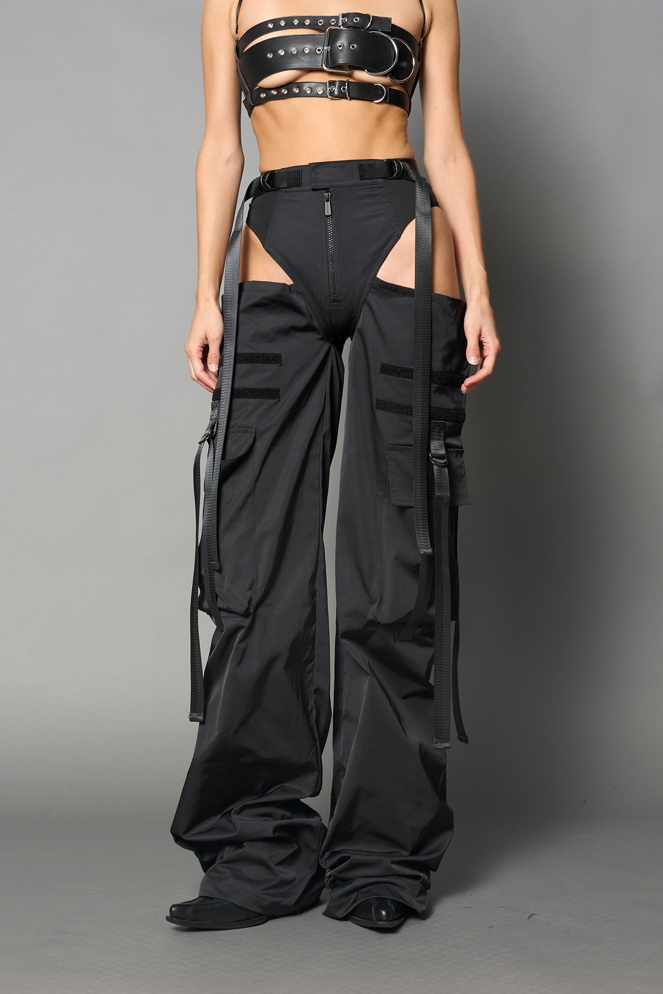 Black nylon cargo trousers with exposed high-cut panty waist, cut-out hips, oversized pockets, and adjustable utility straps – edgy streetwear and festival pants.