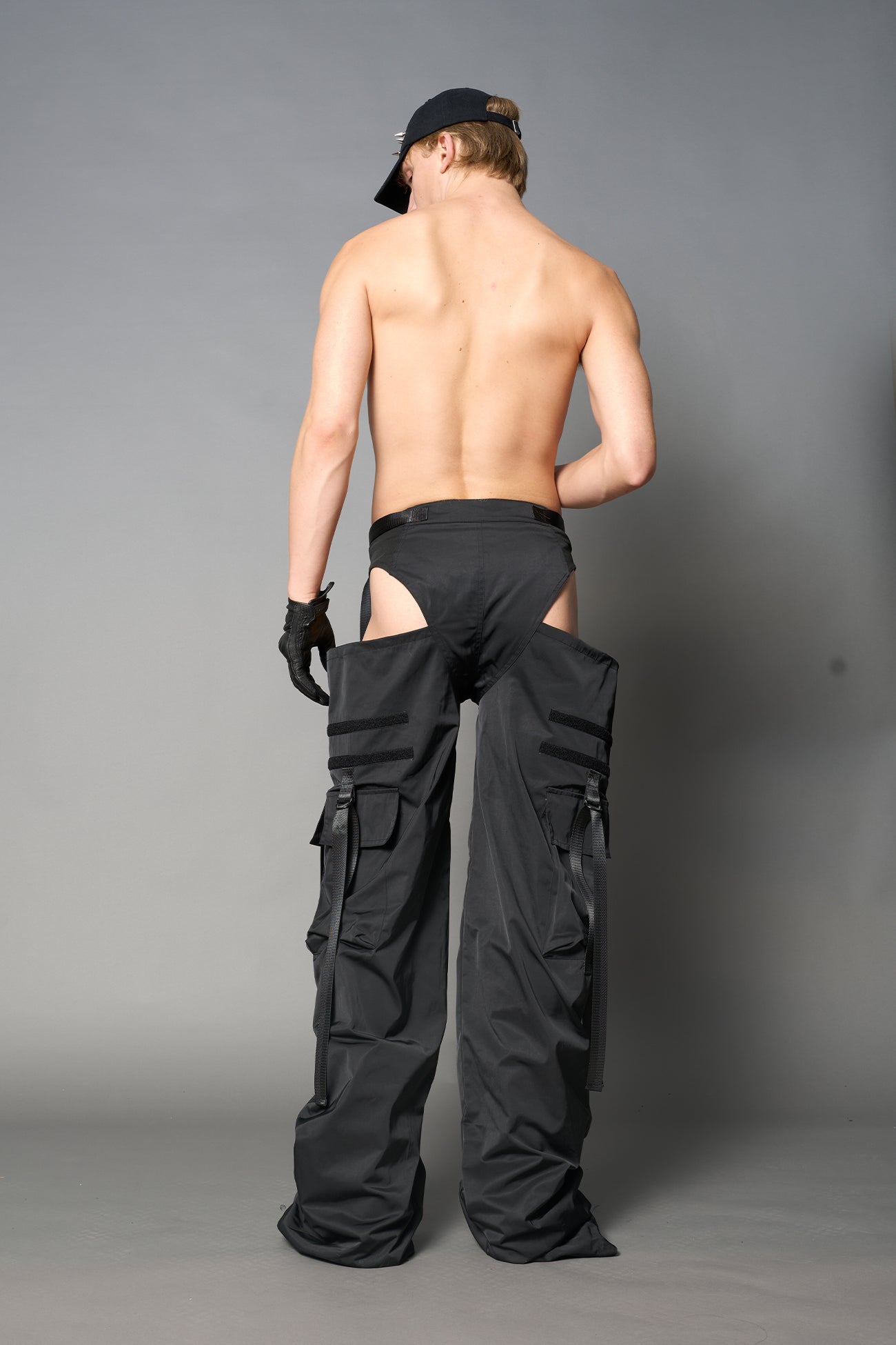 Black nylon cargo trousers with exposed high-cut panty waist, cut-out hips, oversized pockets, and adjustable utility straps – edgy streetwear and festival pants.