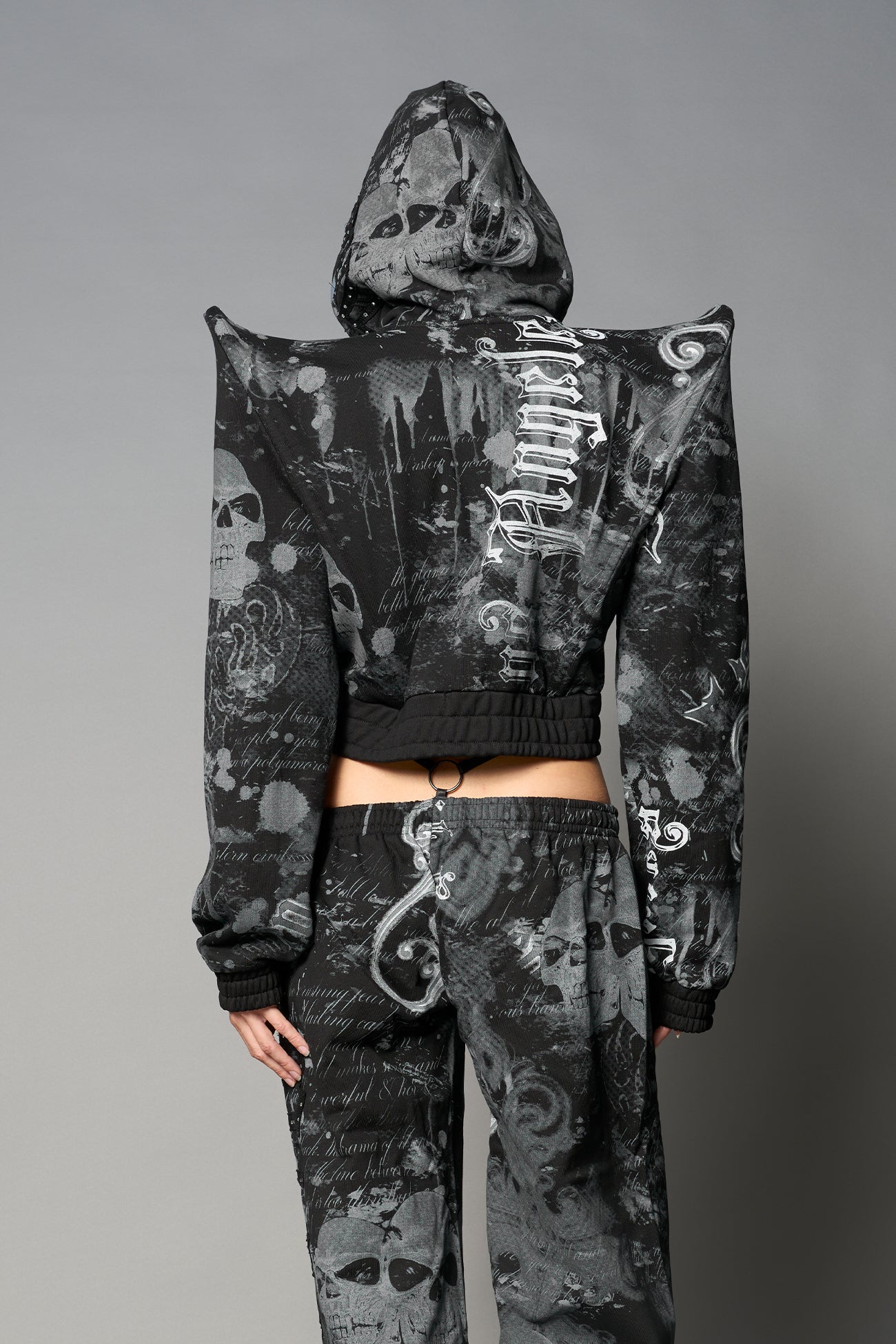 Model wearing a black print cropped hoodie with exaggerated spike shoulders, drawstring hood
