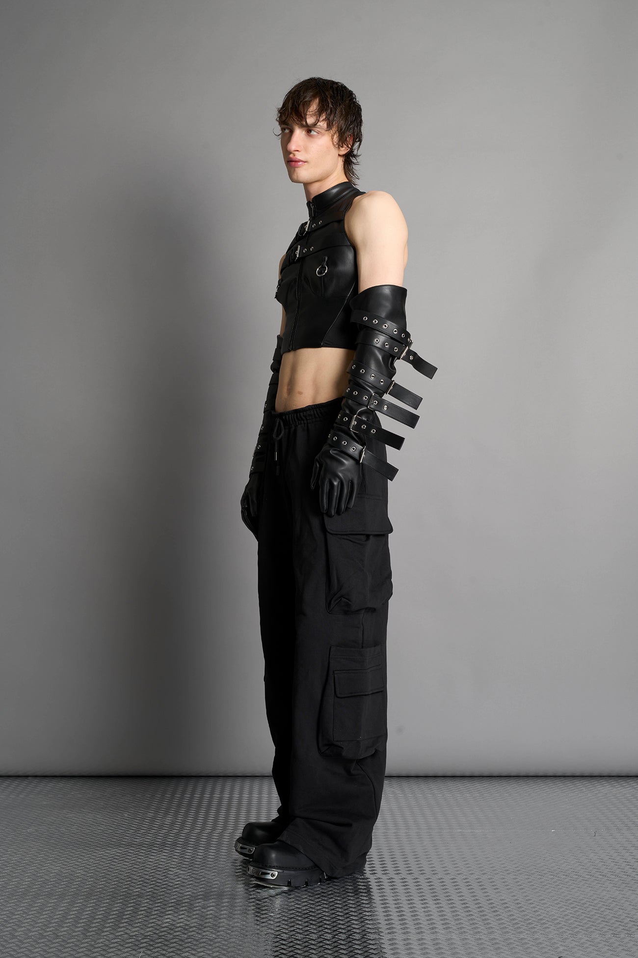Namilia male model Piercing Top in black vegan leather featuring silver metal ring details, cutout design, and edgy Y2K-inspired crop top style. front view
