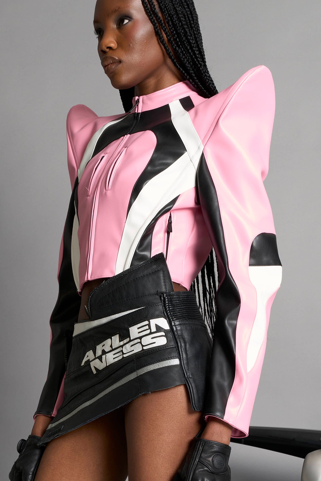 Model wears the pink Namilia Spike Moto Jacket with wire shoulder pads, branded zipper, band collar, zippered breast and waist pockets, motocross-style lines, and black logo rubber tag on the back.