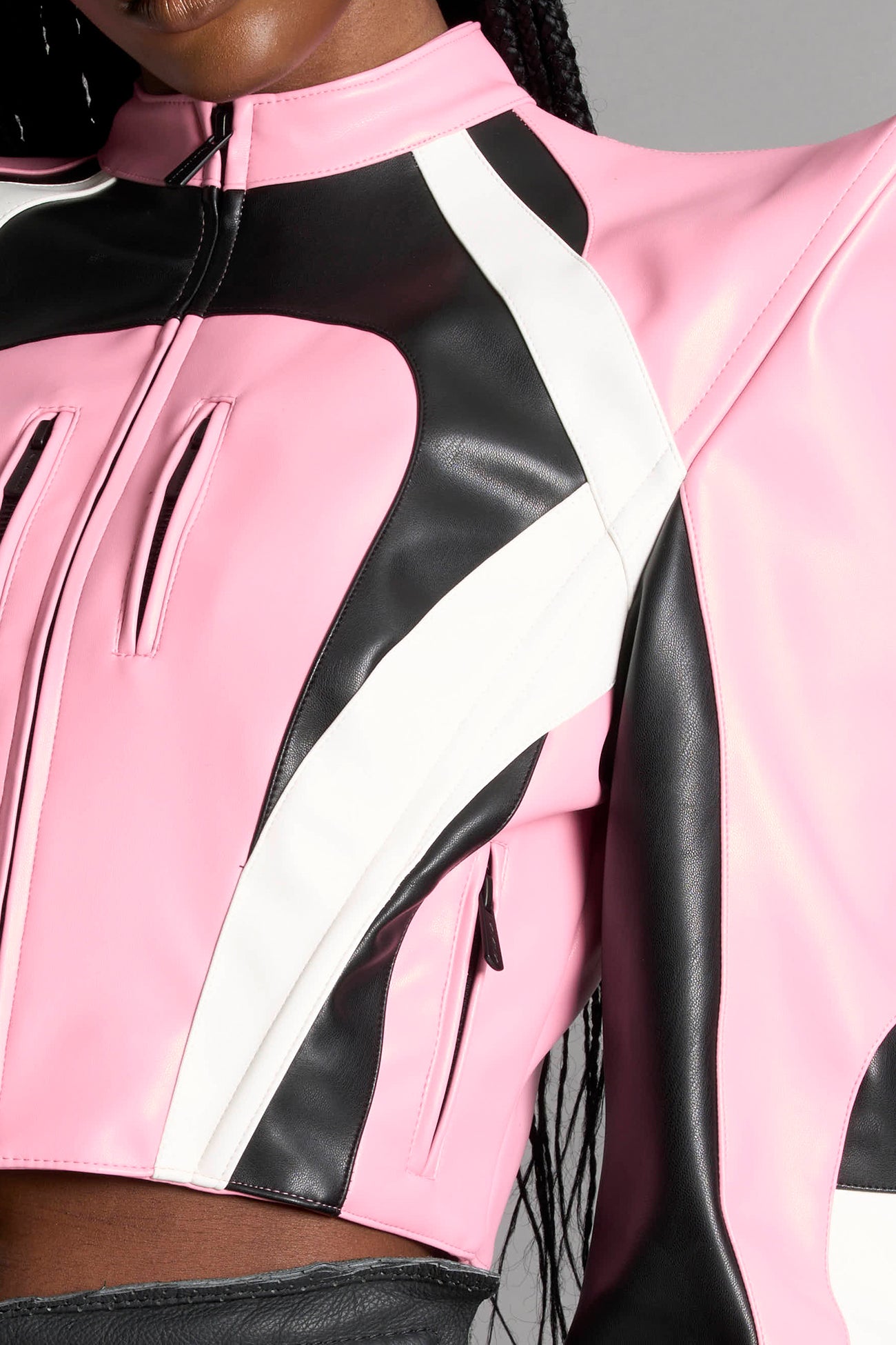Model wears the pink Namilia Spike Moto Jacket with wire shoulder pads, branded zipper, band collar, zippered breast and waist pockets, motocross-style lines, and black logo rubber tag on the back.