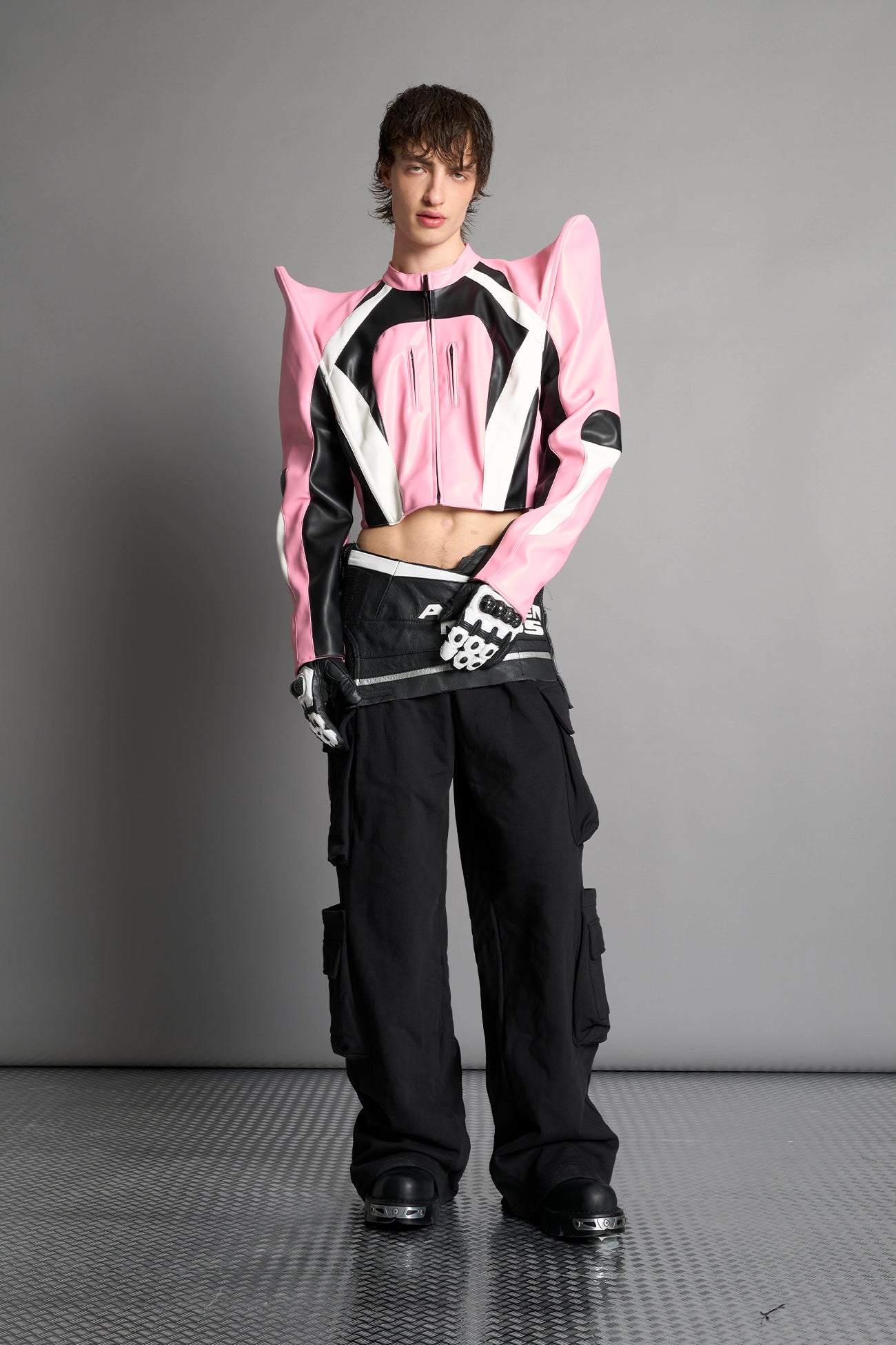 Model wears the pink Namilia Spike Moto Jacket with wire shoulder pads, branded zipper, band collar, zippered breast and waist pockets, motocross-style lines, and black logo rubber tag on the back.