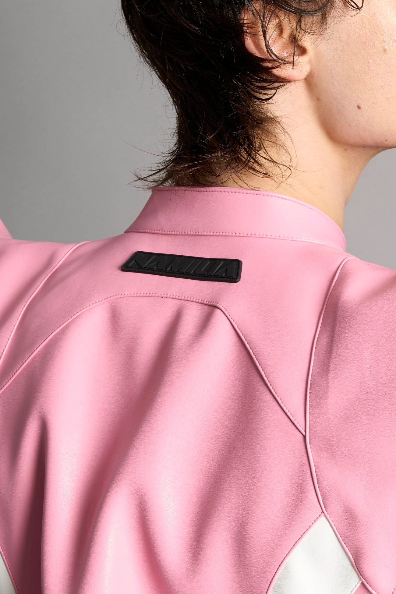 Model wears the pink Namilia Spike Moto Jacket with wire shoulder pads, branded zipper, band collar, zippered breast and waist pockets, motocross-style lines, and black logo rubber tag on the back.